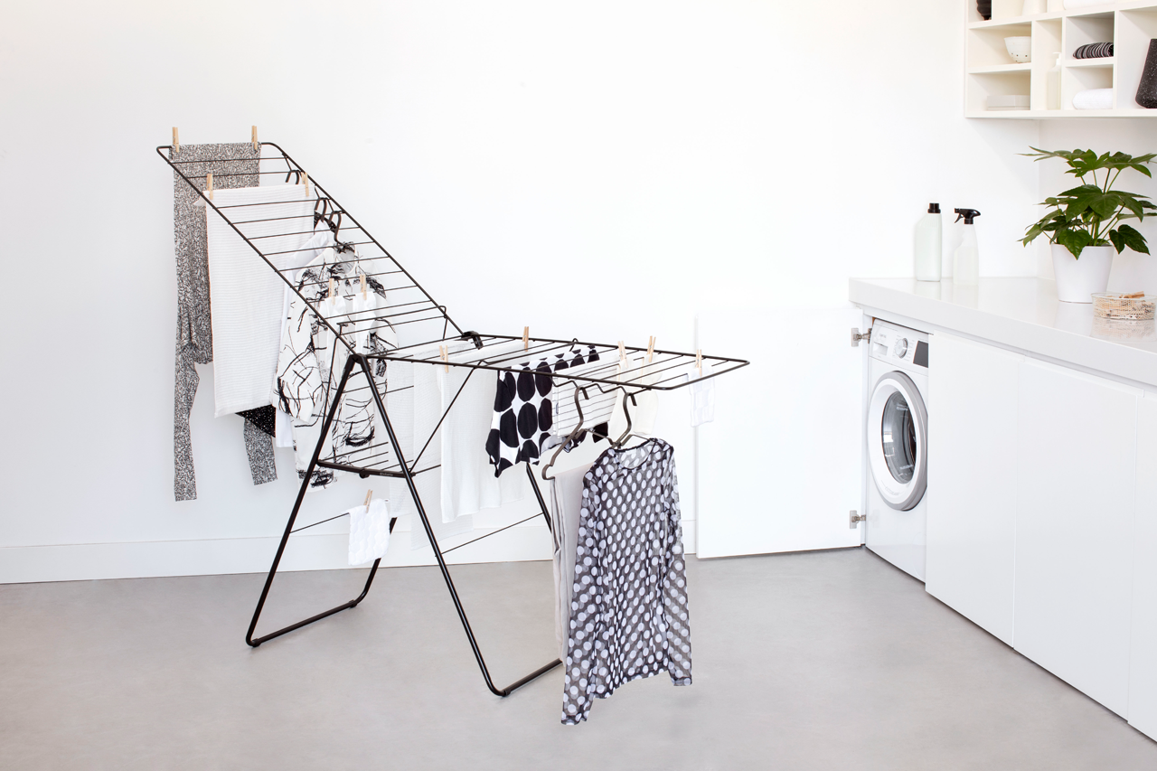 Waschküche mit Wäscheständer, weißer Wand, Waschmaschine. Kleidung hängt und trocknet.