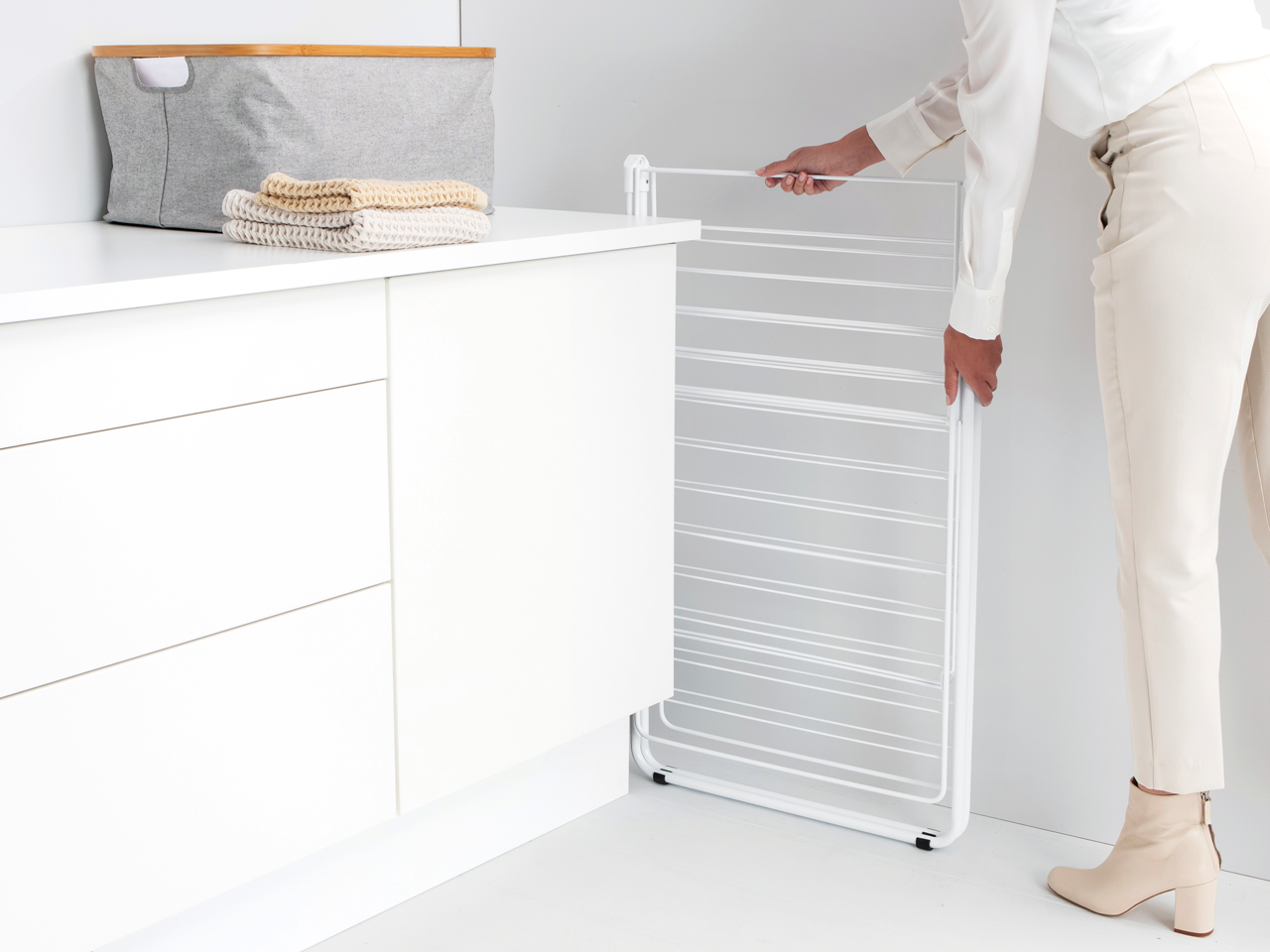 Eine Frau faltet ein weißes Wäschegestell neben einem Schrank mit gefalteten Handtüchern.