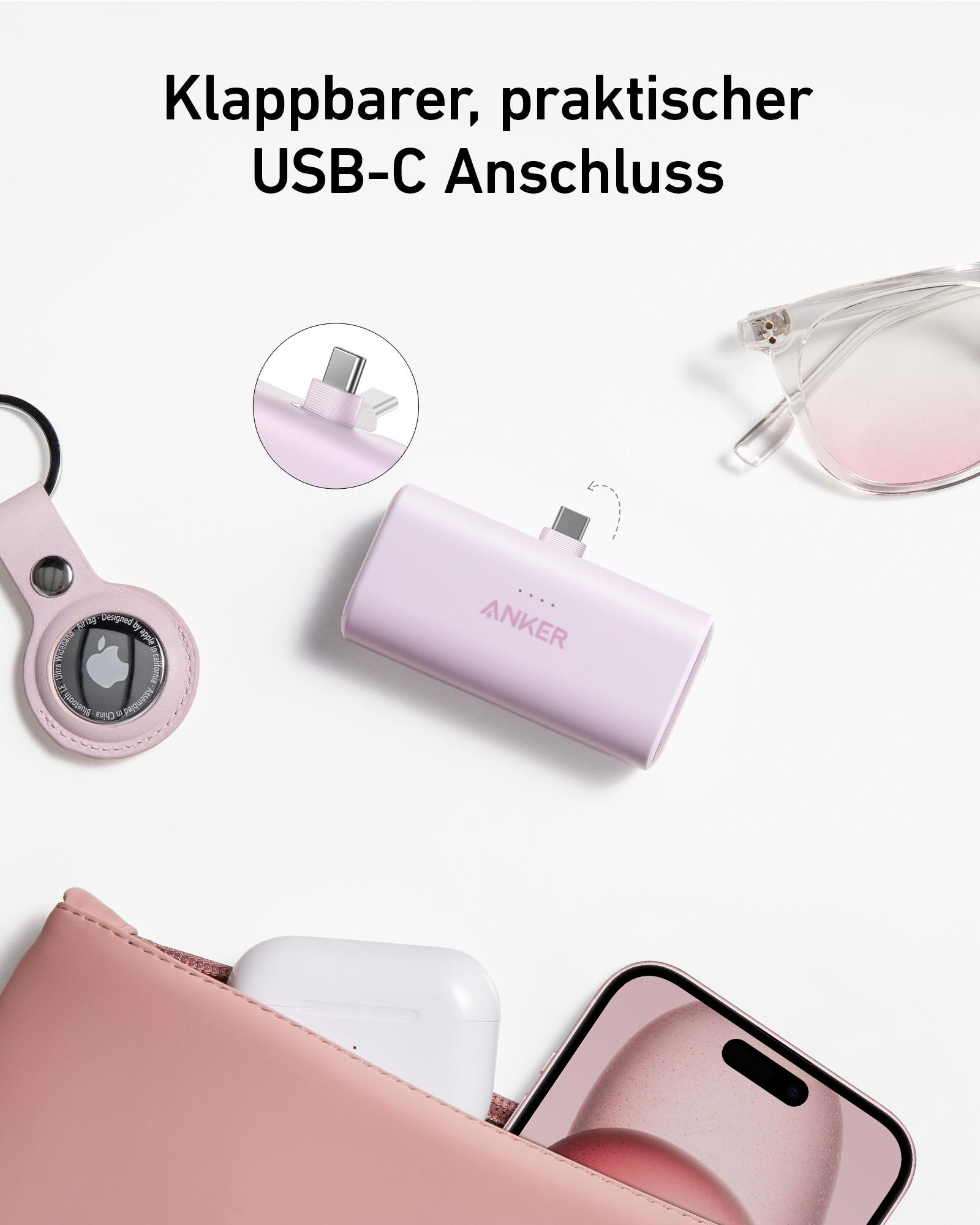 Eine pinkfarbene Anker Powerbank mit USB-C-Anschluss, in der Nähe einer Geldbörse, eines Telefons und Ohrhörern.