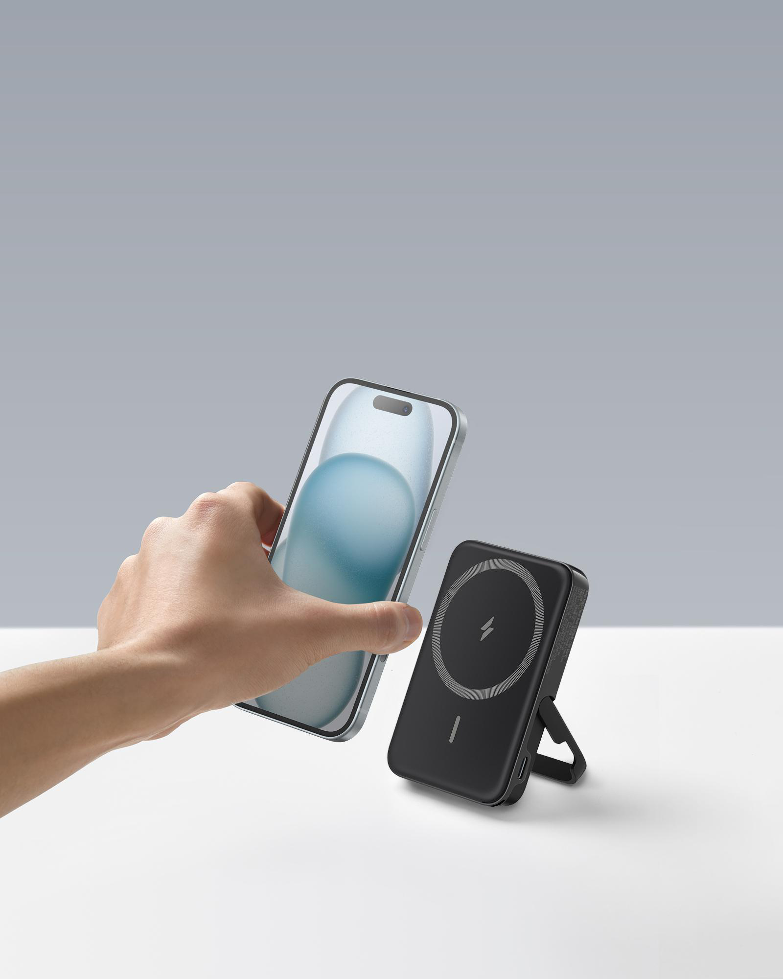 Hand, die Telefon in der Nähe einer schwarzen Powerbank mit Ständer und Ladesymbol hält.
