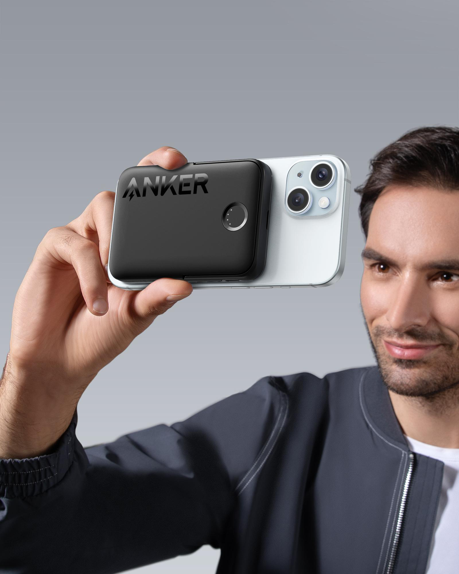Ein Mann hält eine schwarze Anker Powerbank neben einem weißen iPhone.