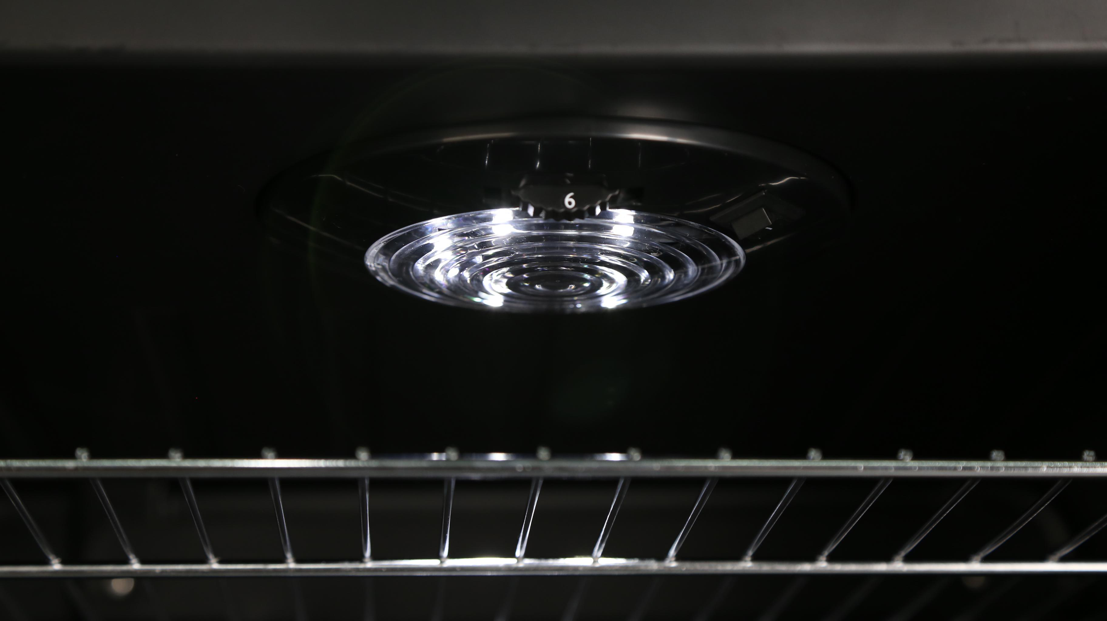 Ein Backofeninnenraum mit Licht und einem Metallrost. Das Innere ist schwarz.