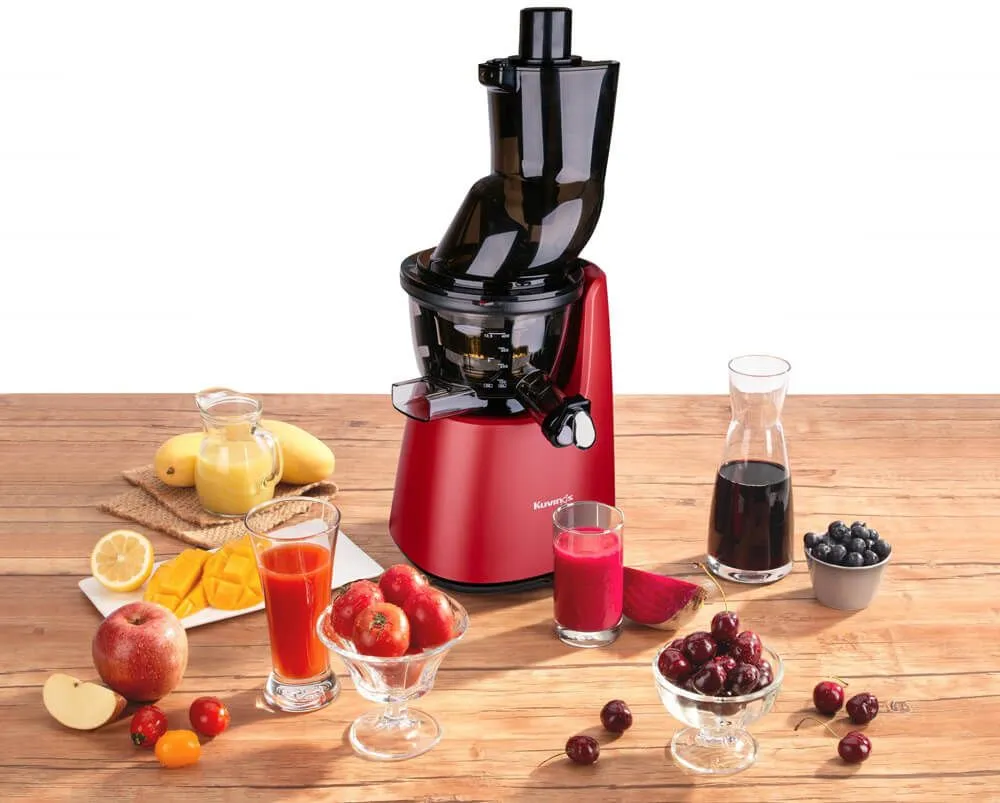 Czerwona wyciskarka do soku z różnymi owocami i sokami na drewnianym stole. Zawiera mango, jabłka, wiśnie i buraki.