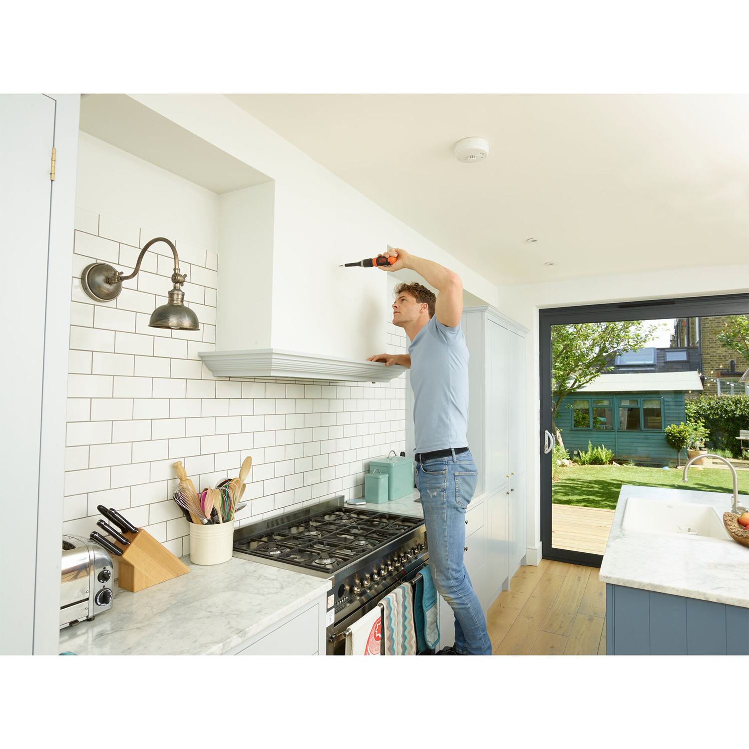 Un uomo usa un trapano per installare una cappa aspirante in cucina, con vista esterna soleggiata.