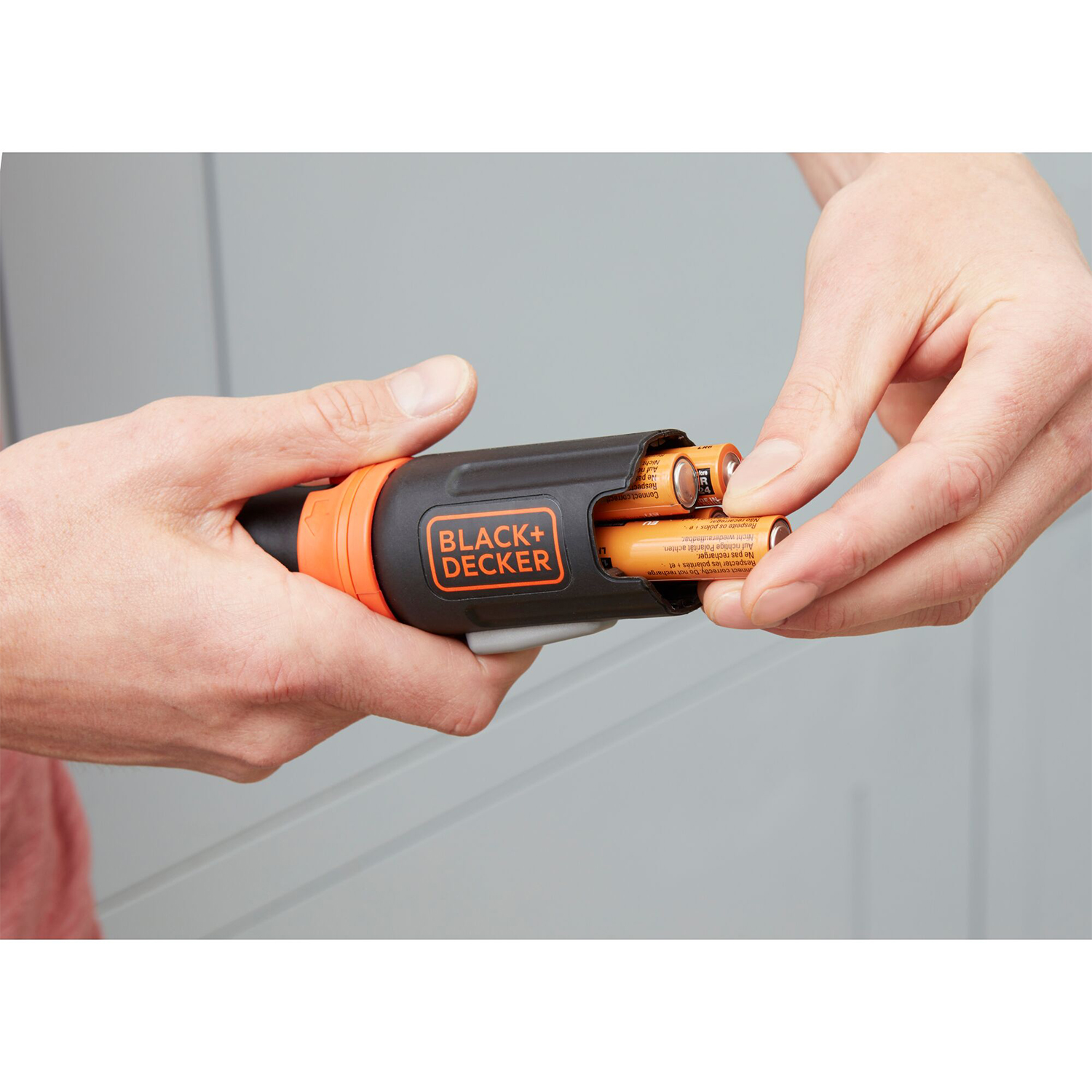 Mani che inseriscono le batterie in un cacciavite Black and Decker. Nero e arancione.