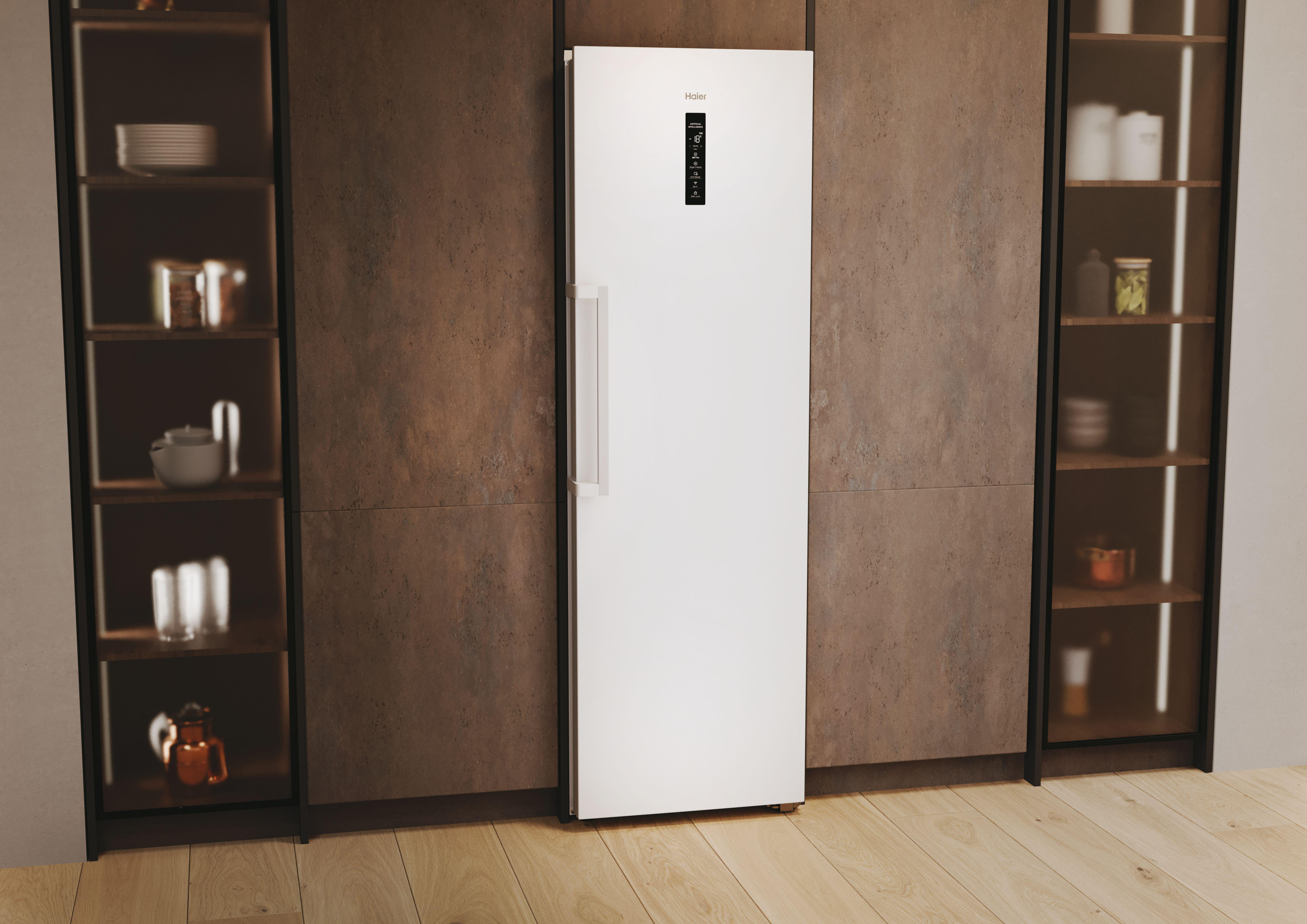 Ein weißer Haier-Kühlschrank steht zwischen Holzschränken. Der Türgriff ist sichtbar.