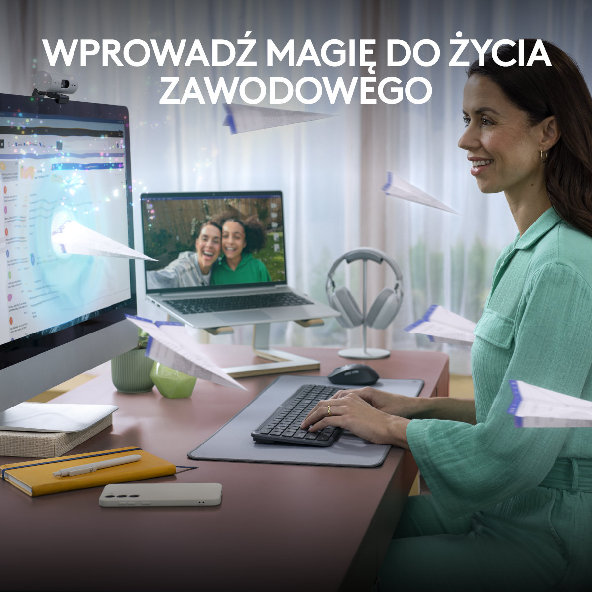 Kobieta przy biurku, latające papierowe samoloty, monitory i laptop.