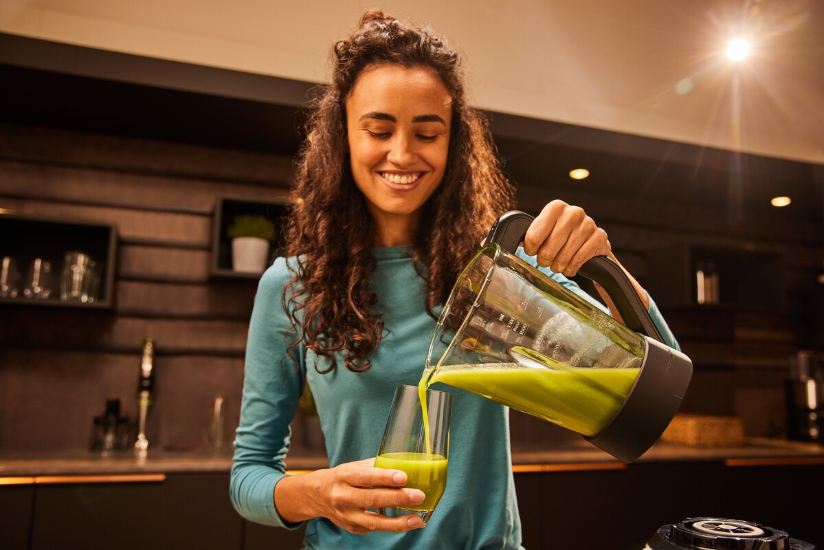Frau gießt grünen Saft in ein Glas. Kücheninterieur.