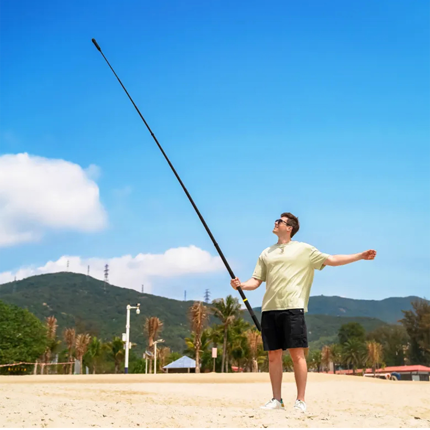 Uomo sulla spiaggia tiene lungo palo nero verso cielo blu.