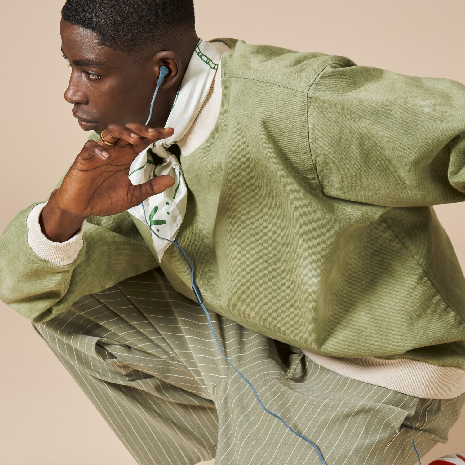 Un homme portant une veste verte et un pantalon à rayures, tenant des écouteurs bleus.