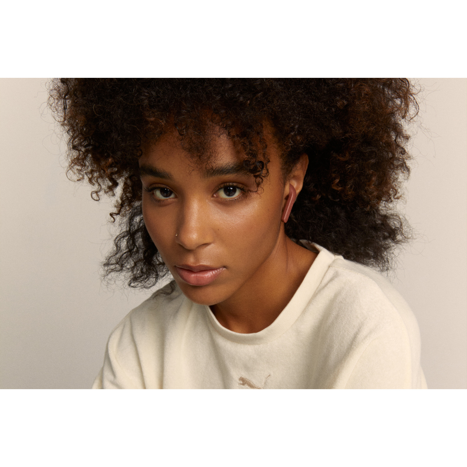 Une femme aux cheveux bouclés portant des écouteurs roses, regardant la caméra.