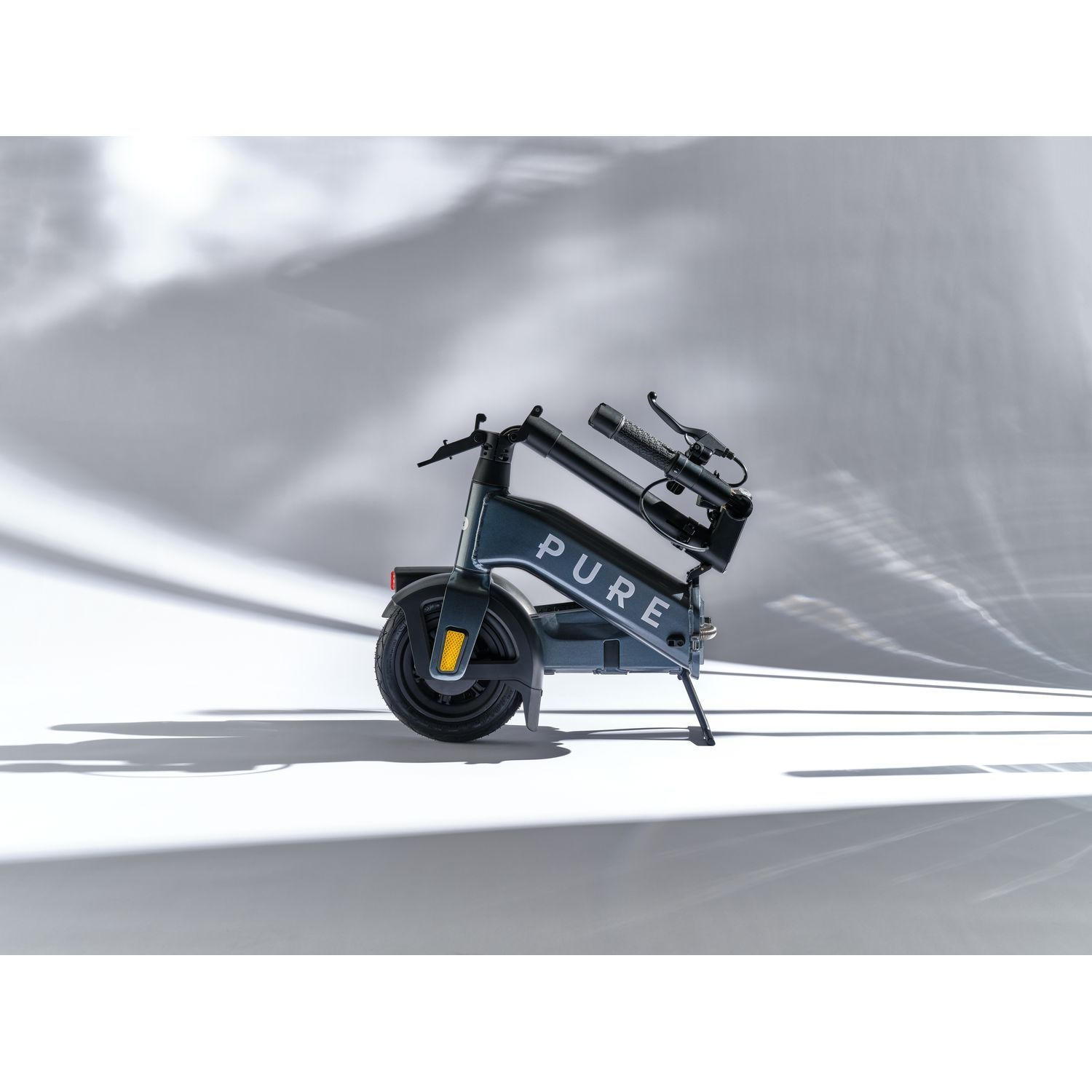 Trottinette électrique pliée, noire et grise, garée sur une surface blanche. La trottinette est en studio.