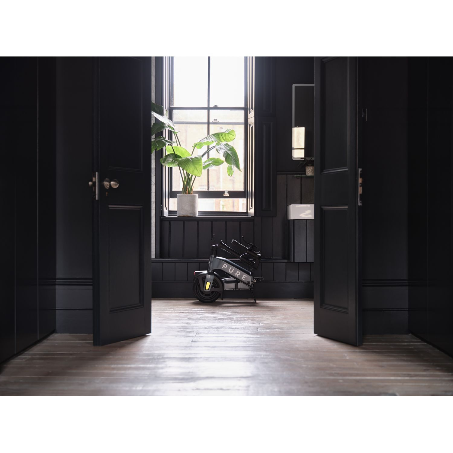 Intérieur moderne avec une trottinette électrique et une plante. Murs sombres et plancher en bois.