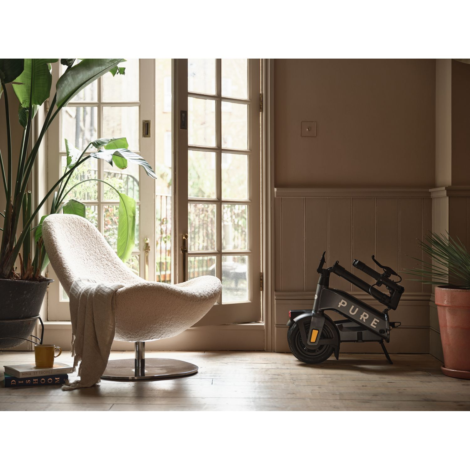 Une pièce avec un scooter, une chaise et des plantes. Le scooter porte la mention 'PURE'.
