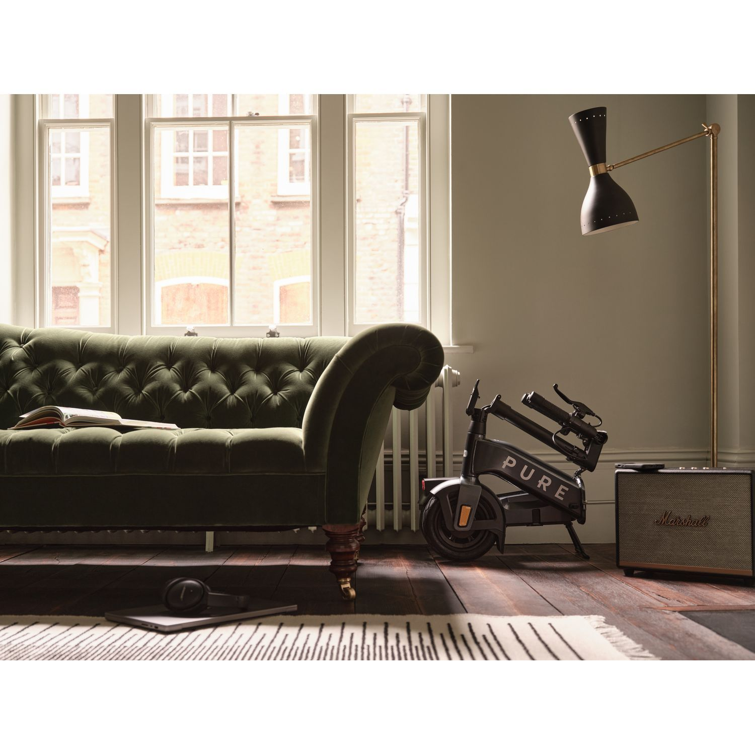 Salon avec canapé vert, vélo et lampe. Un tapis et des enceintes sont également visibles.