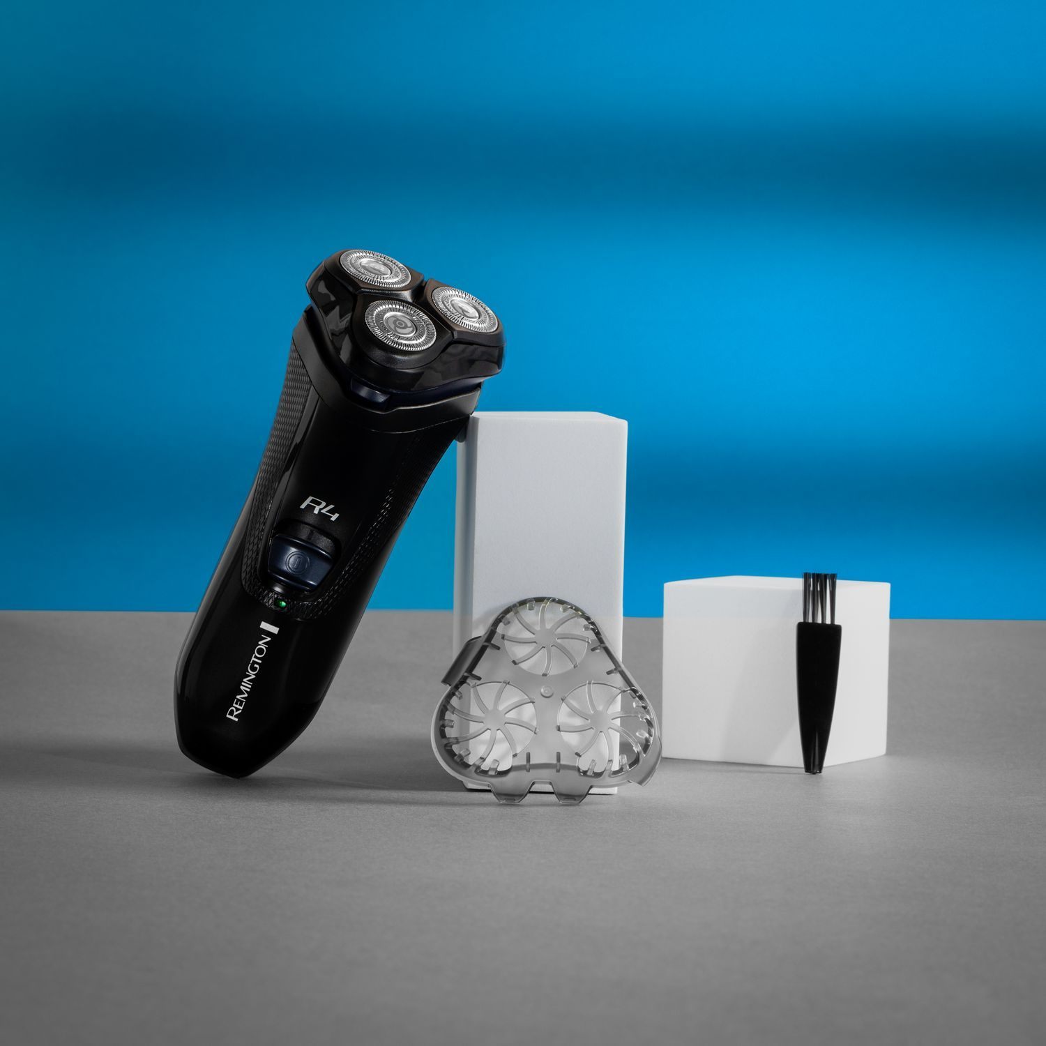 Black Remington R4 shaver with accessories on gray surface, blue background.