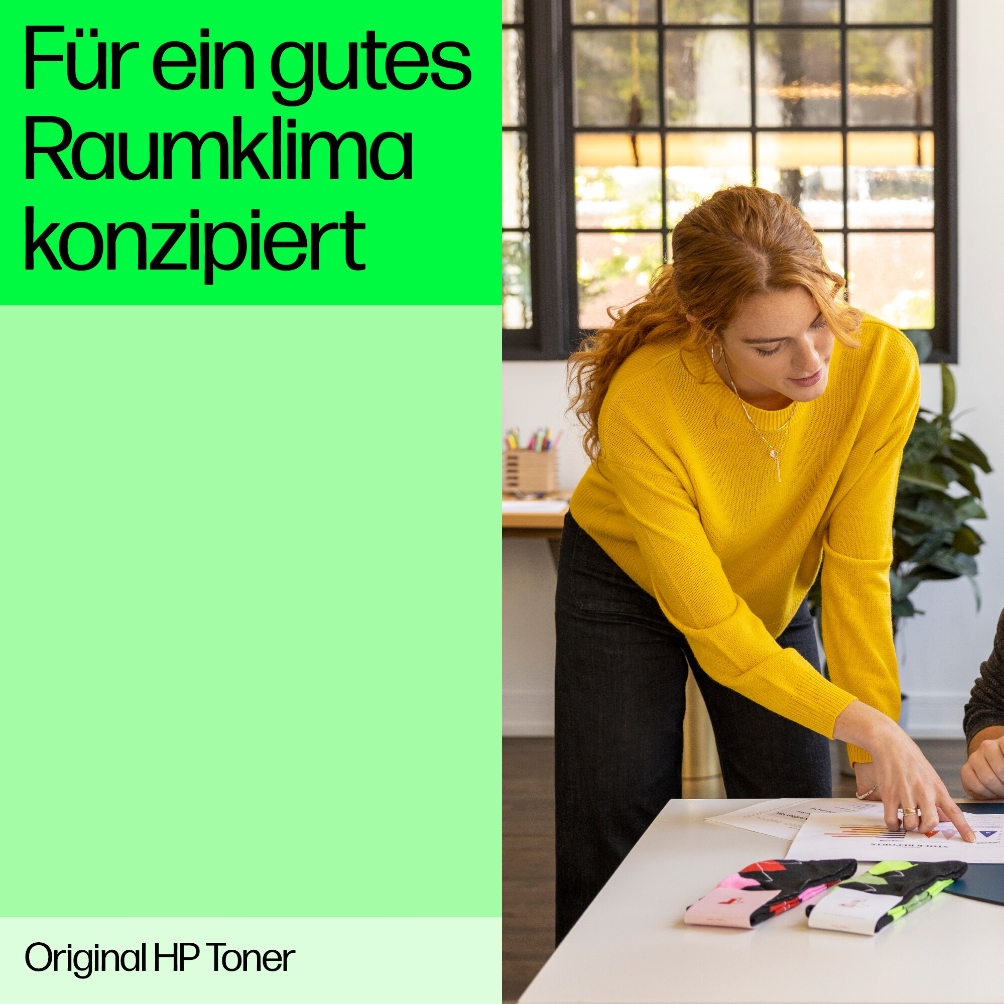 Frau in gelbem Pullover zeigt auf Dokument. Schreibtisch mit Papieren und Stiften.
