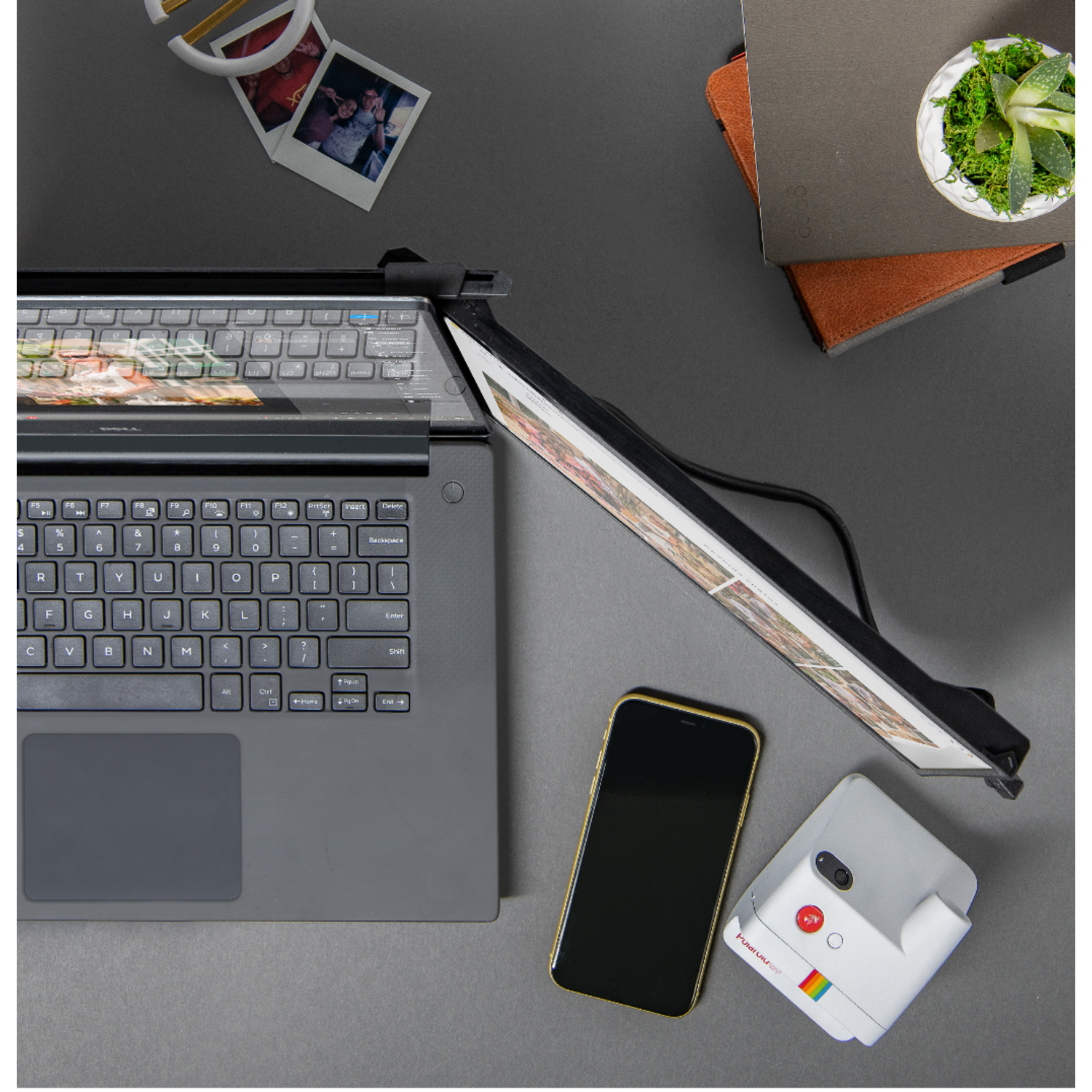 Top view of a laptop, phone, polaroid camera, and other objects on a gray surface.