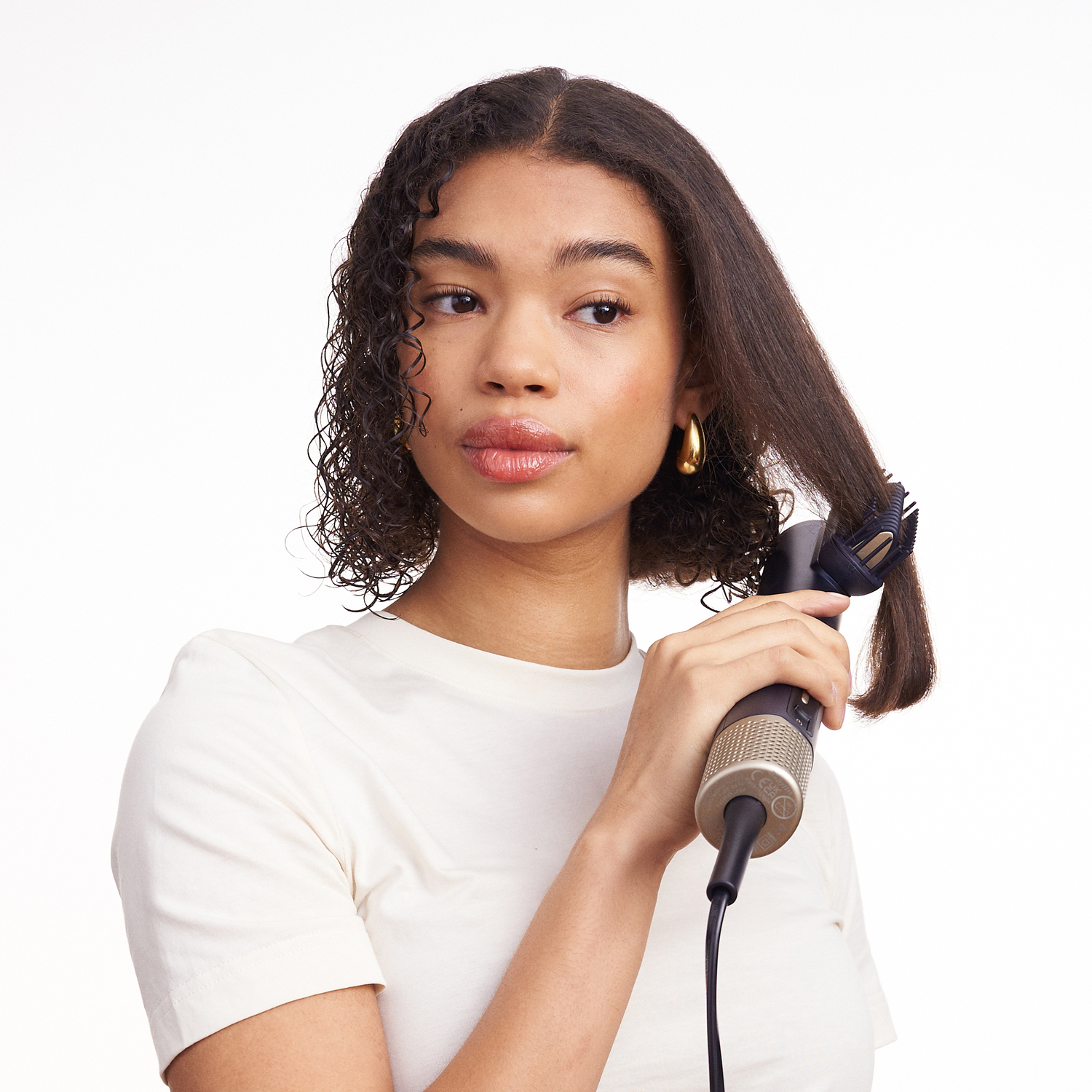 A woman is styling her hair with a hair styler.
