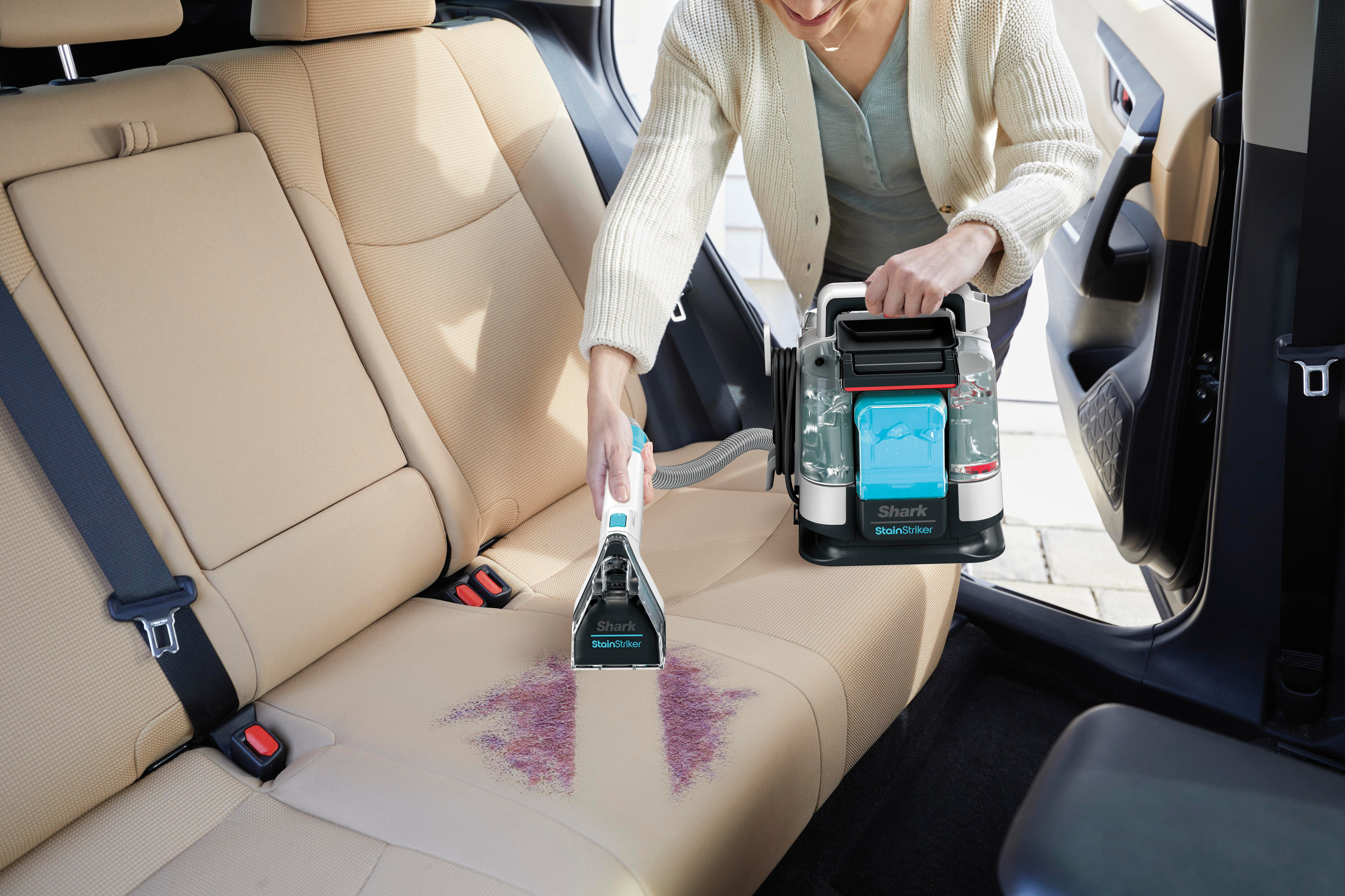 Frau reinigt Autositz mit Shark StainStriker. Schaum- und Wasserspray, Reinigungskopf.