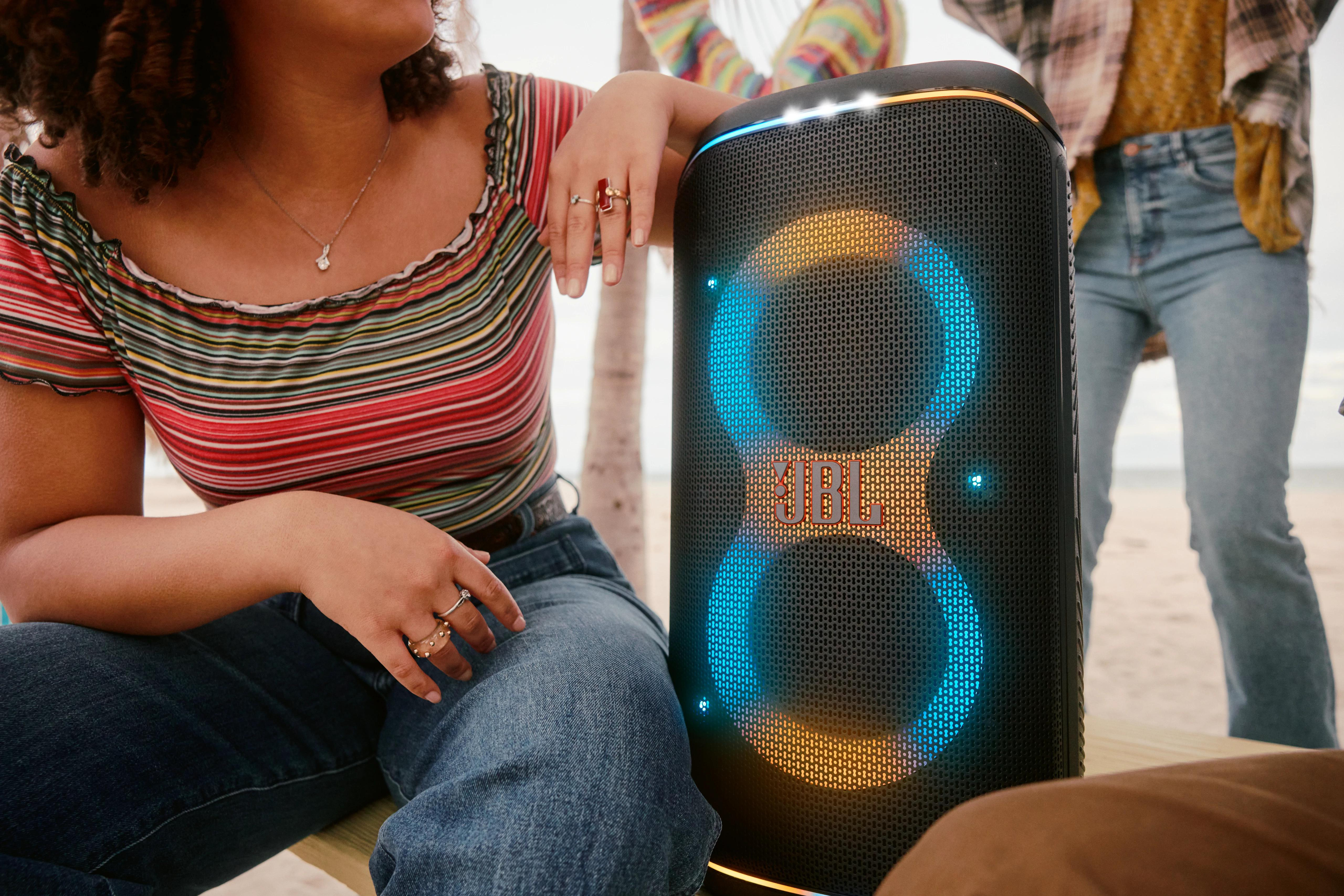 Eine Gruppe von Leuten mit einem großen JBL-Lautsprecher am Strand, mit hellen Lichtern.