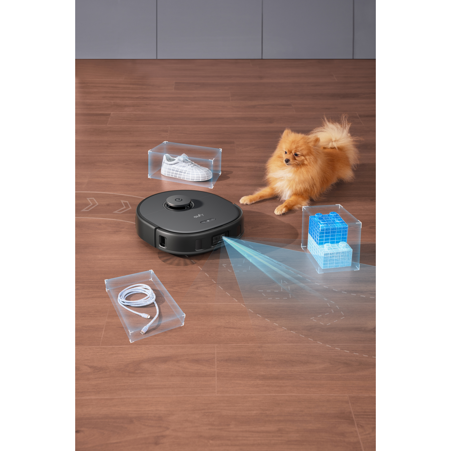 Un aspirateur robot noir avec une lumière bleue, un chien, une chaussure et un câble dans des boîtes.