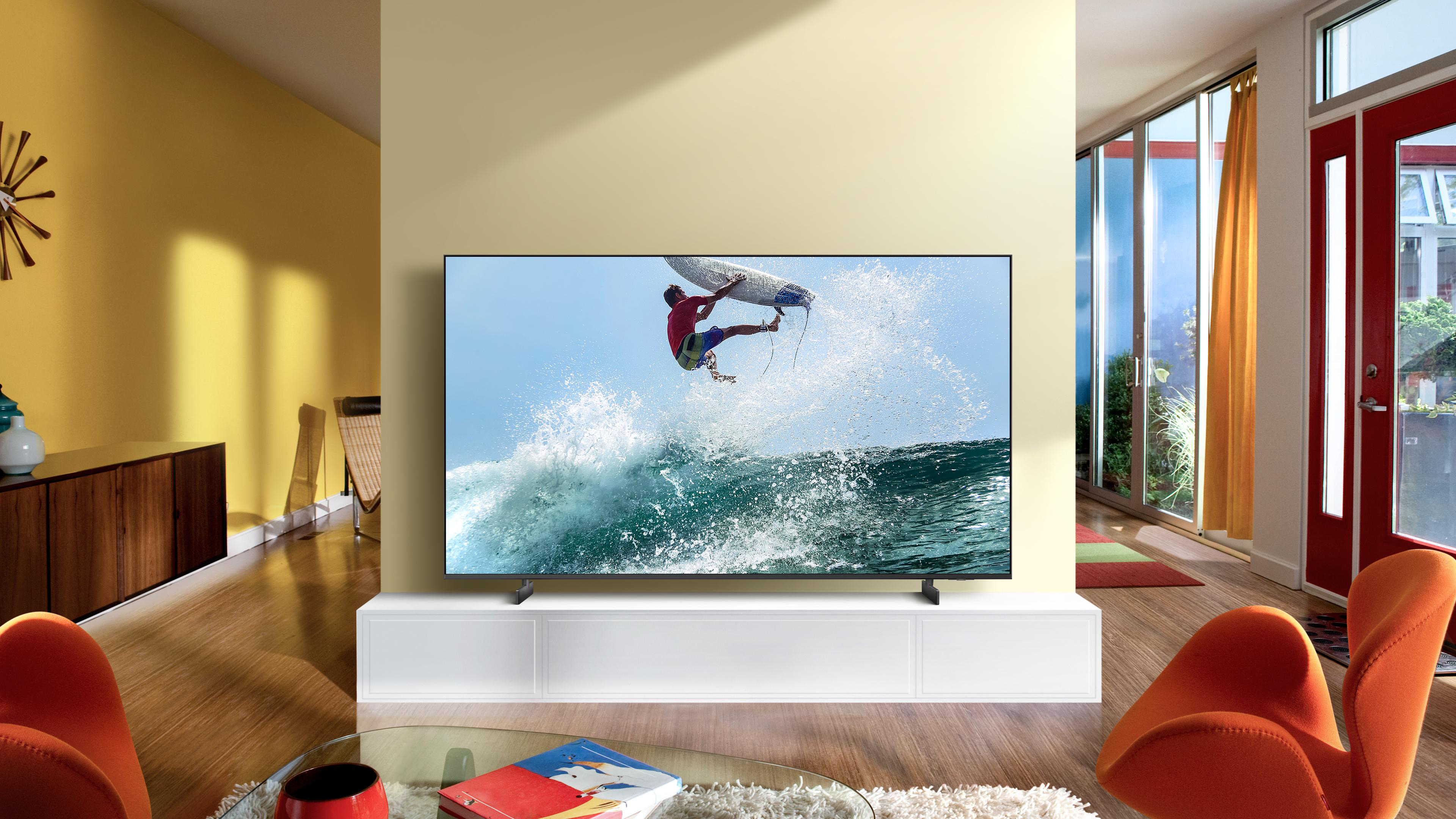 Wohnzimmer mit TV, der einen Surfer zeigt. Orangefarbene Stühle und eine gelbe Wand sind sichtbar.