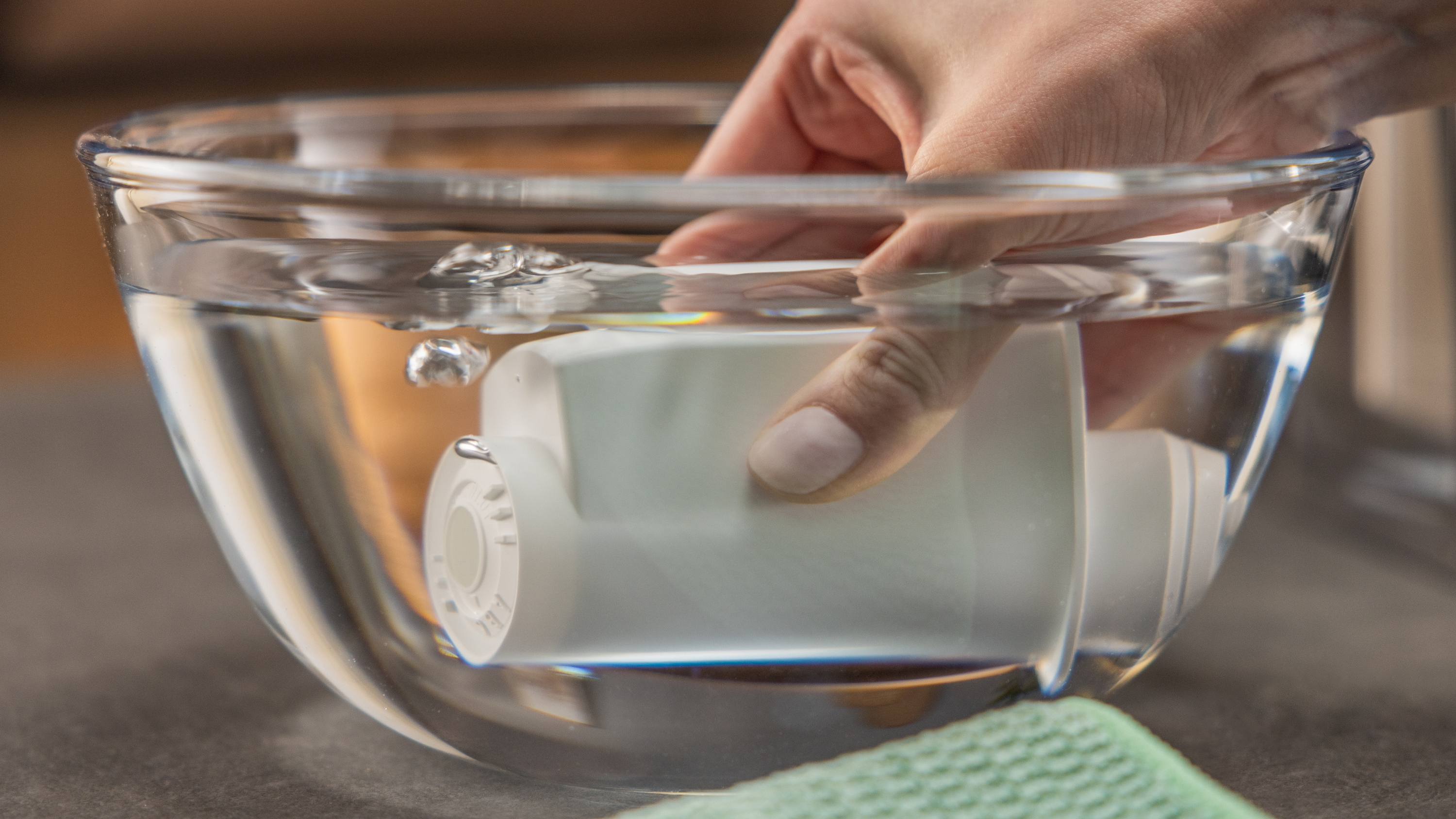 Eine Hand taucht einen weißen Wasserfilter in eine klare Glasschüssel mit Wasser.