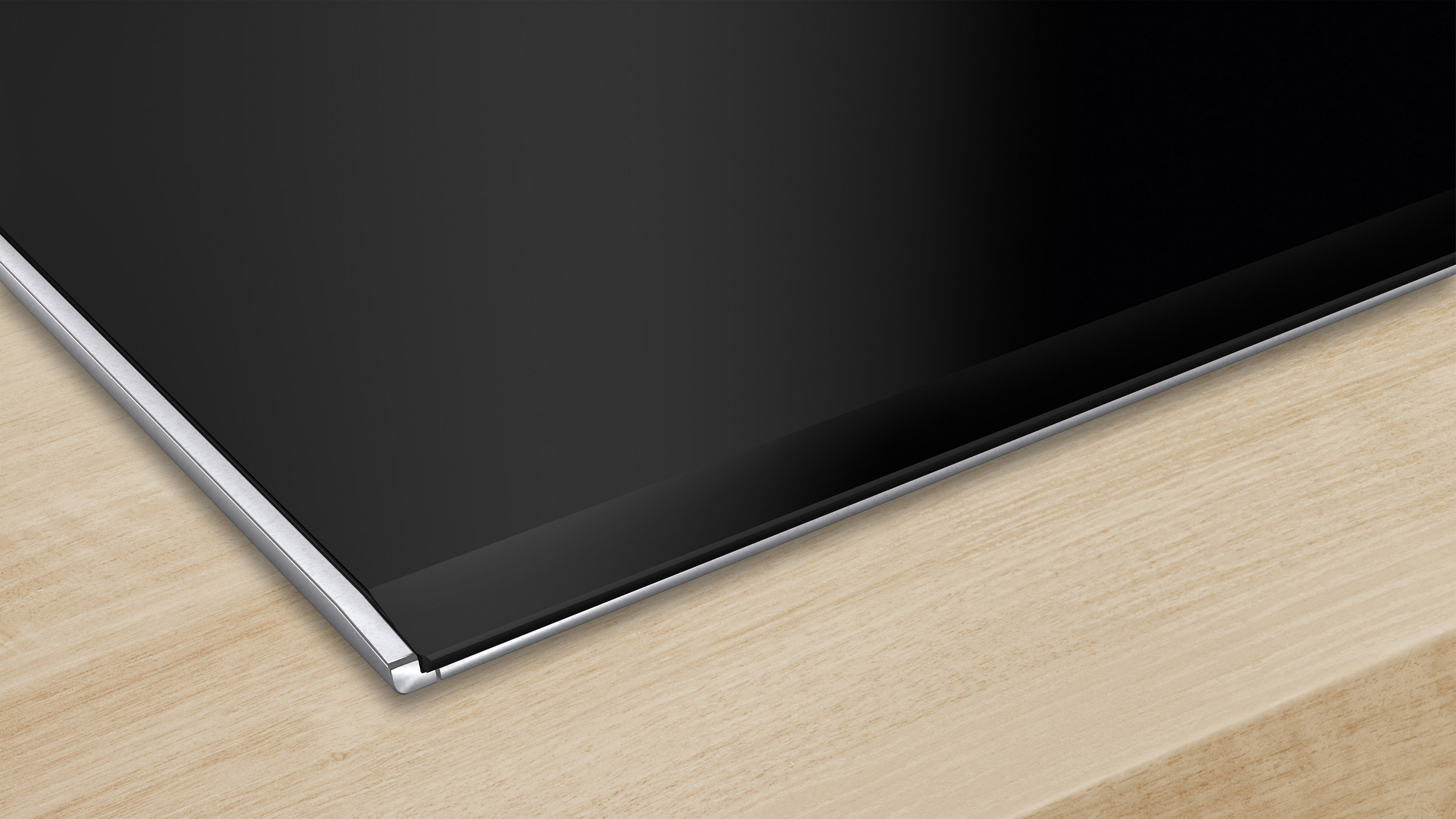 Zbliżenie czarnej, prostokątnej płyty grzewczej ze srebrną obwódką na jasnej drewnianej powierzchni.