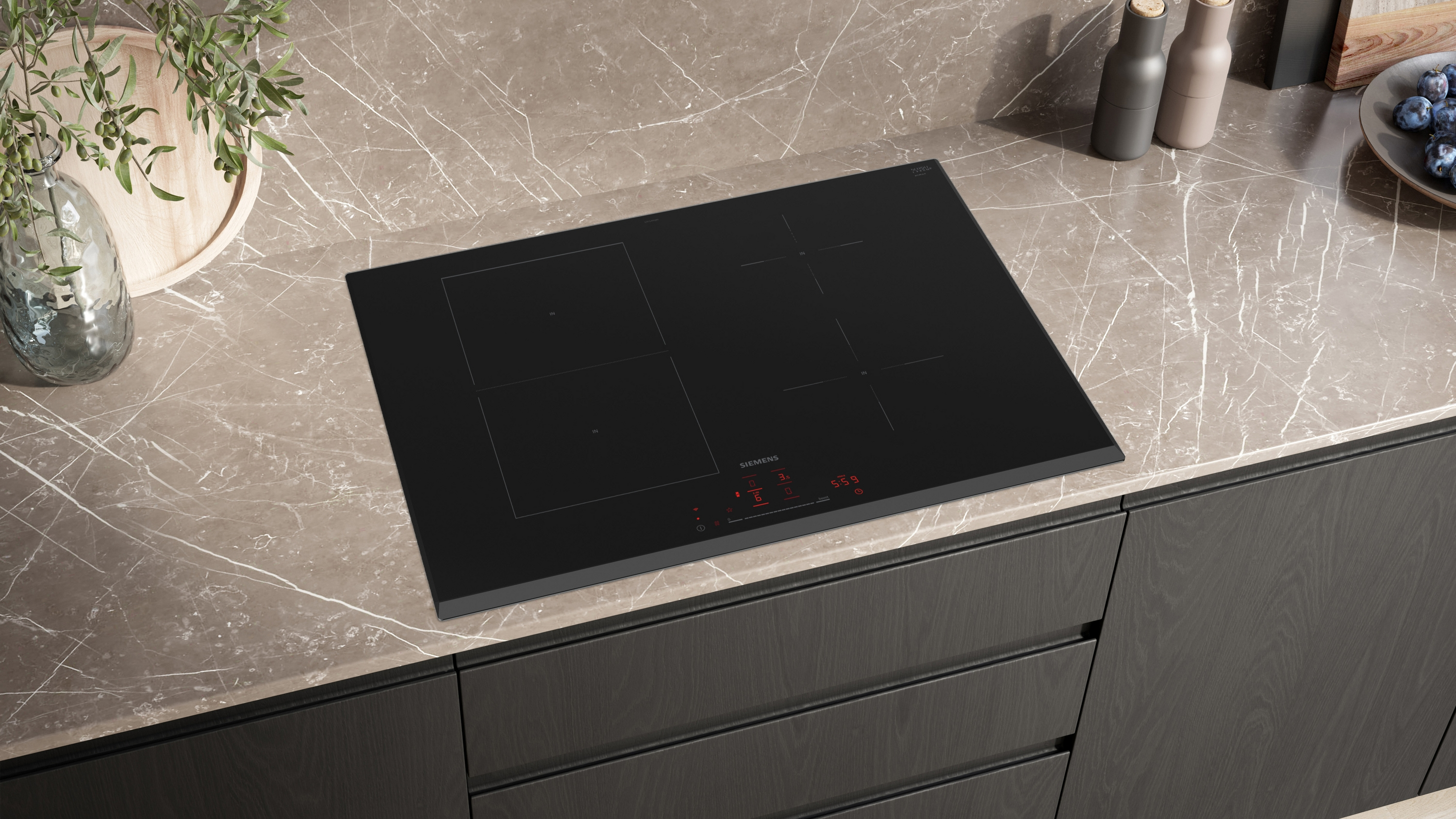 A black stovetop with four burners. A light gray countertop and black cabinets in the background.