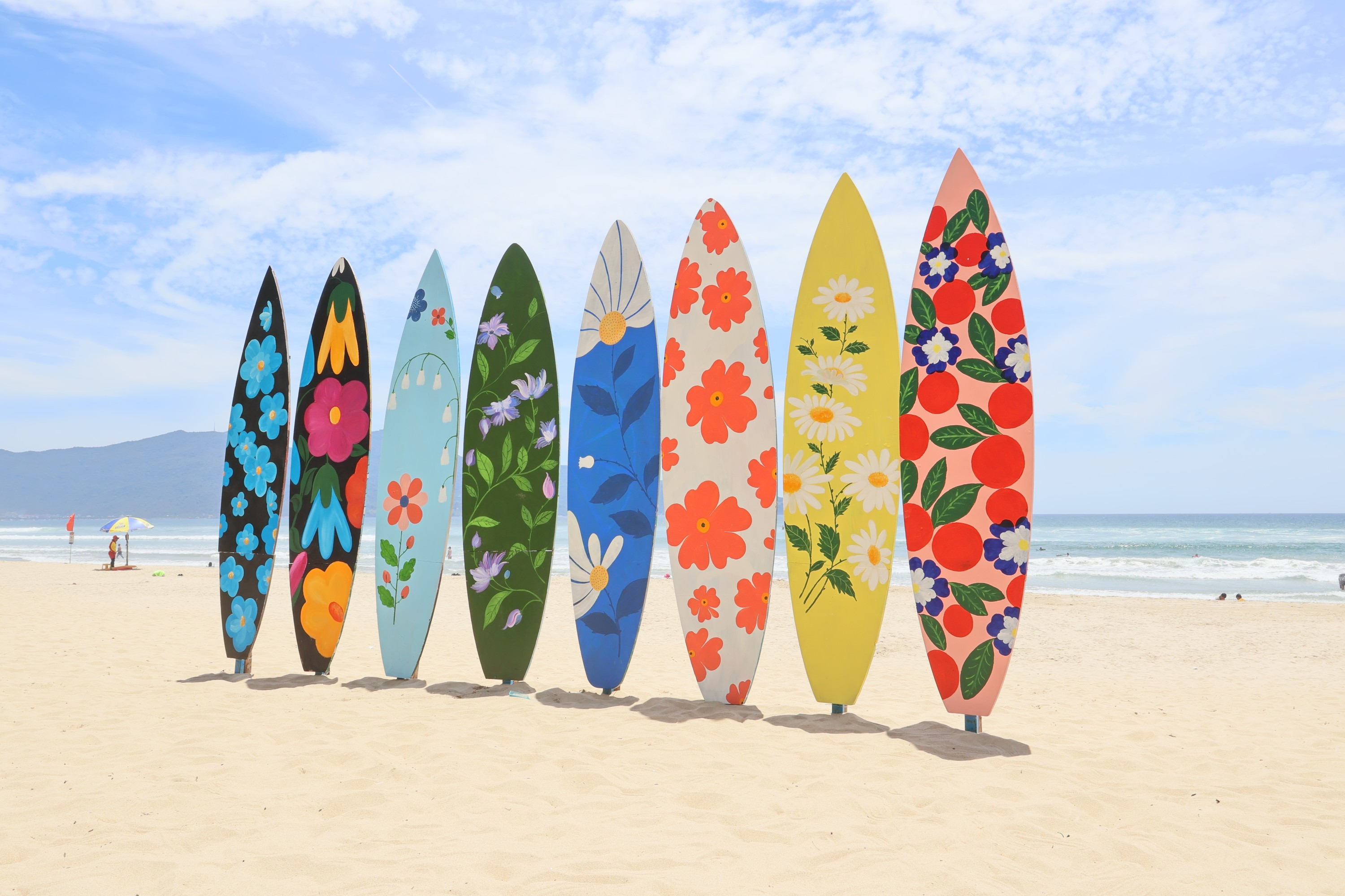 Eine Reihe farbenfroher Surfbretter mit verschiedenen floralen Designs an einem Sandstrand.
