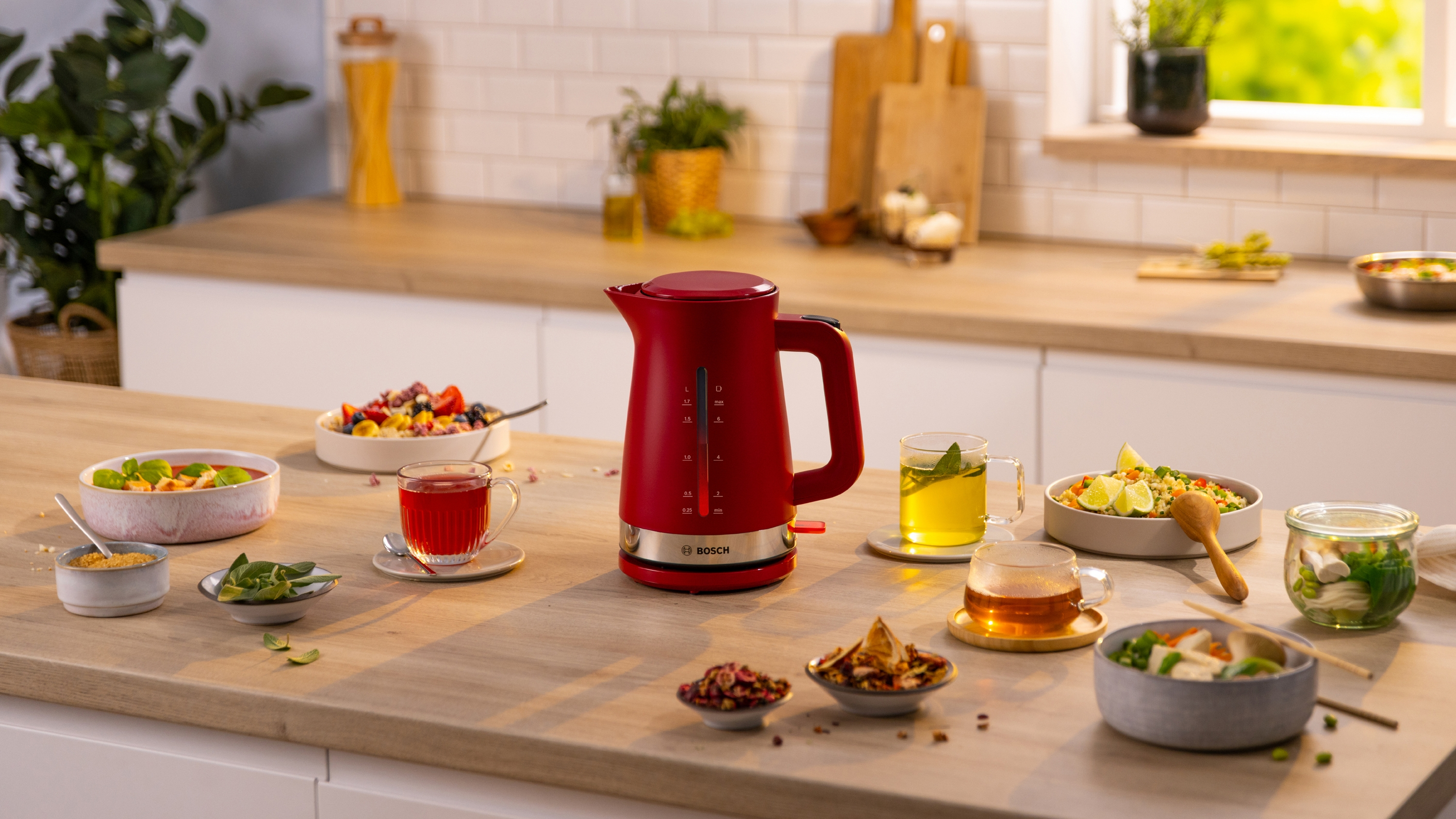 Roter Wasserkocher, umgeben von Schalen mit Essen und Getränken auf Holz. Küche.