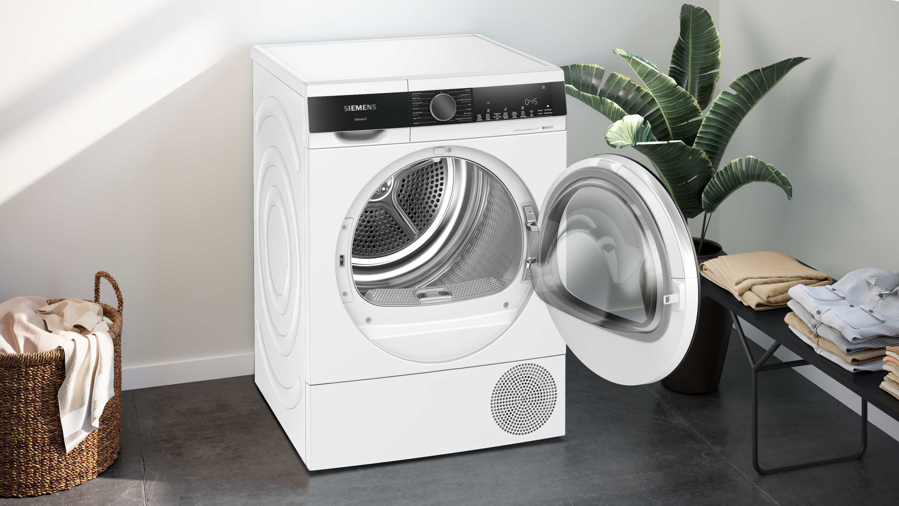 White dryer with open door, laundry basket, and plant.