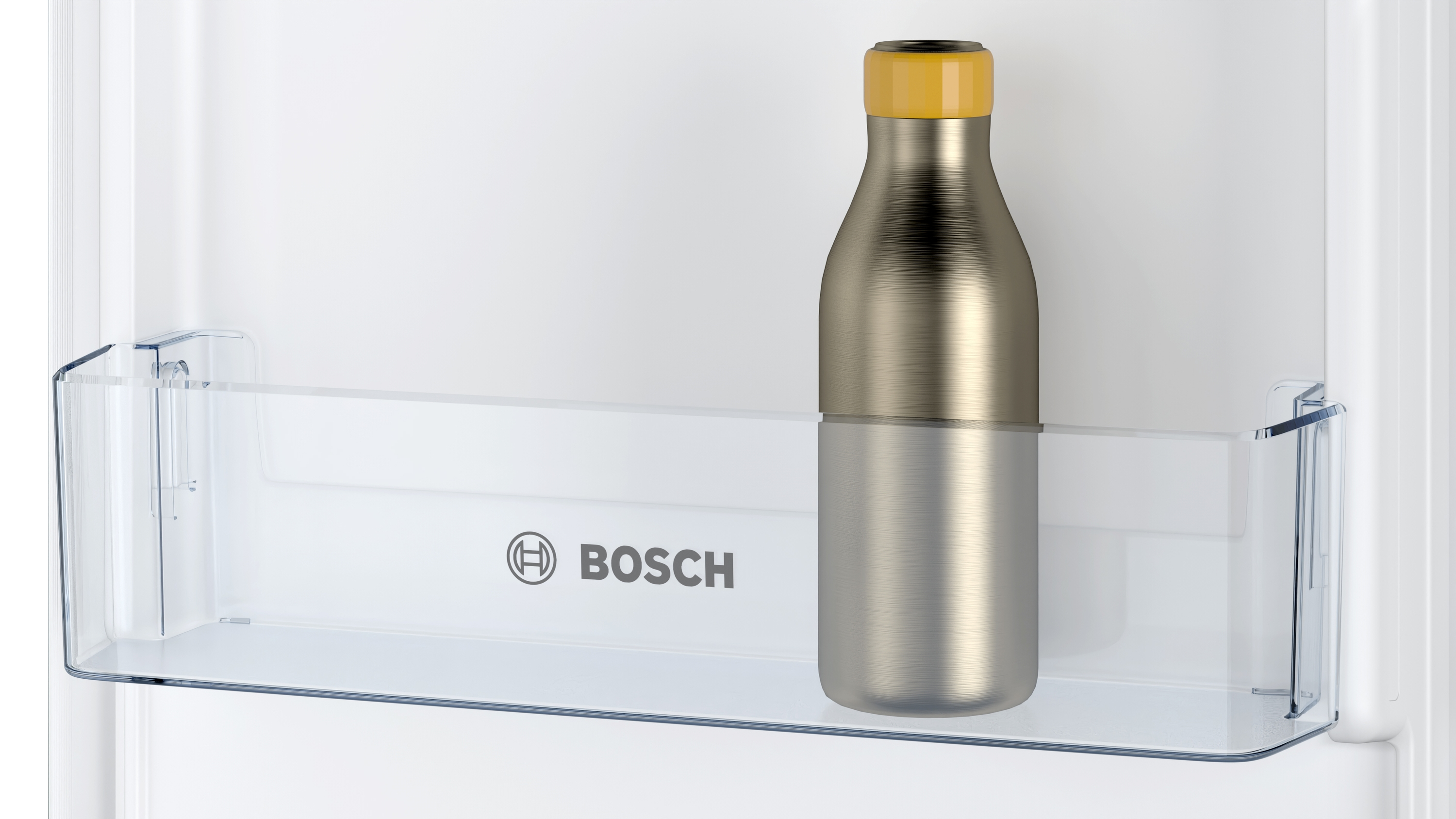 Eine silberne Flasche mit gelbem Deckel steht in einem Kühlschrank auf einem Regal.