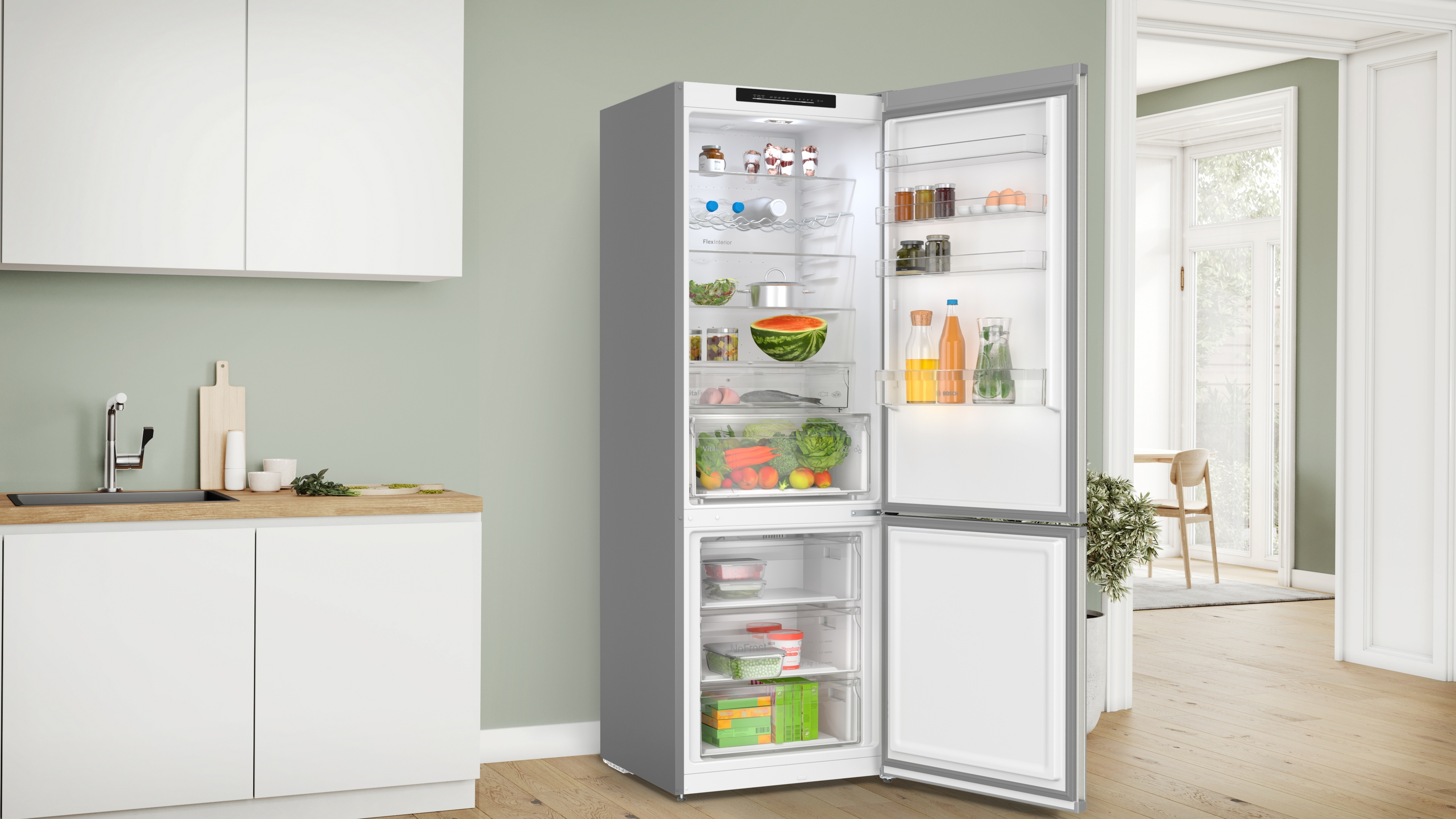 Geöffneter Kühlschrank in einer Küche. Der Kühlschrank ist grau, mit Essen im Inneren. Die Küche hat weiße Schränke.