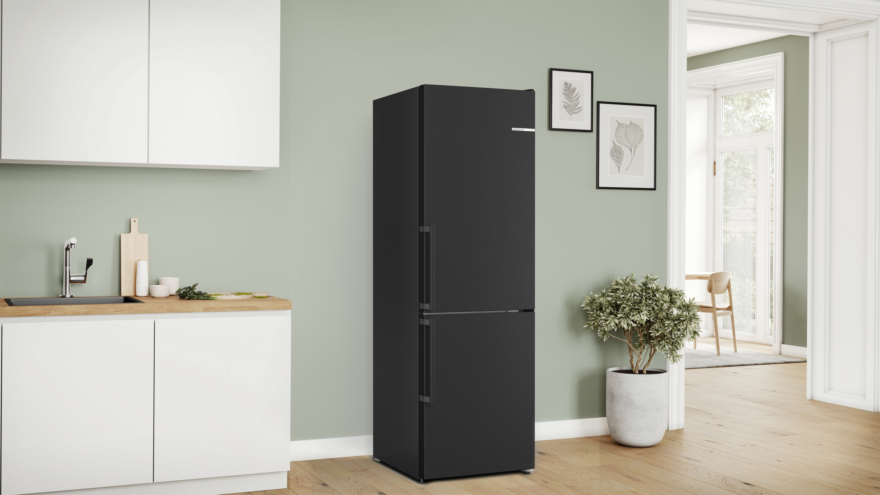 Geschlossener schwarzer Kühlschrank in einer Küche mit weißen Schränken und einer Pflanze.