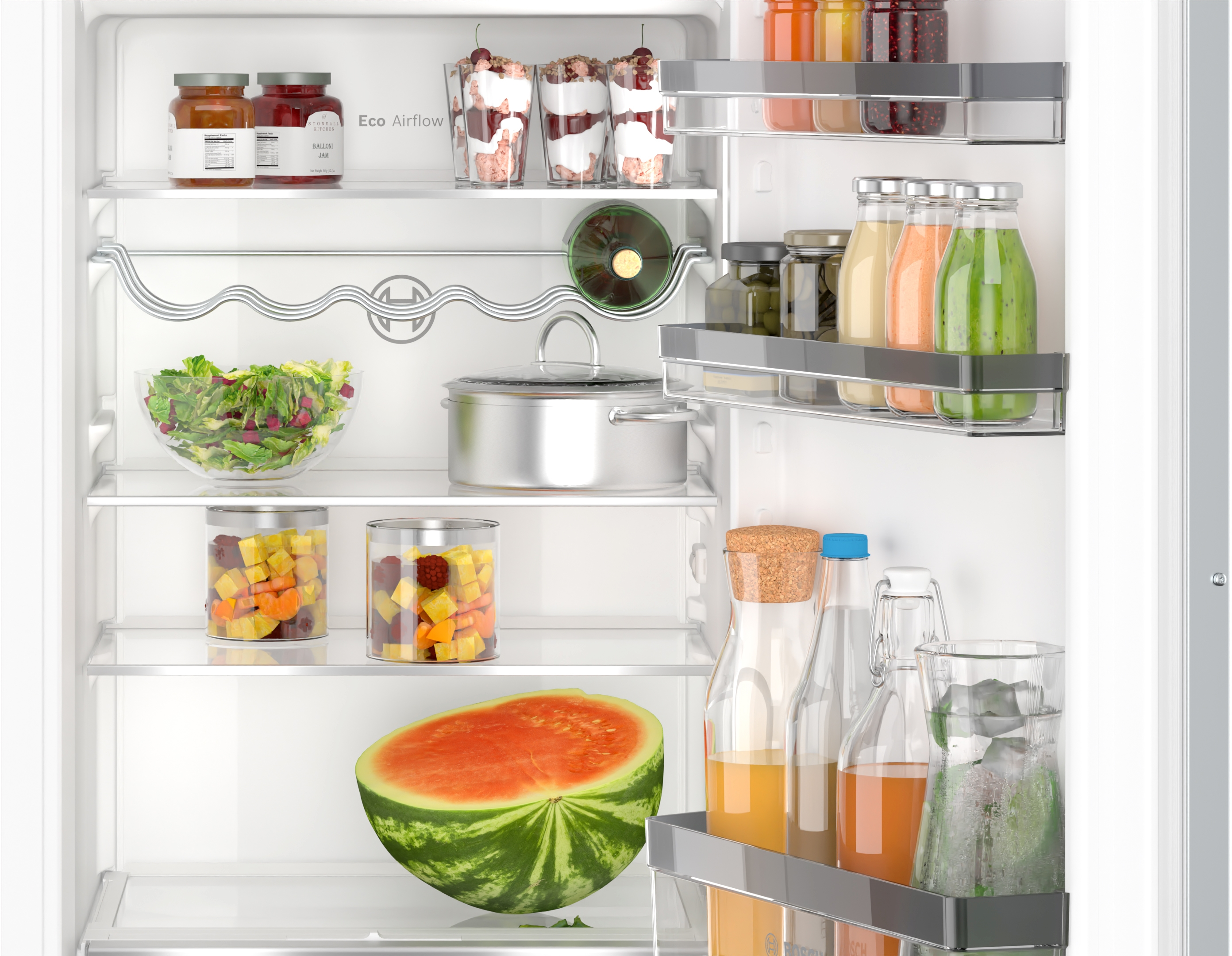 Im Kühlschrank, gefüllt mit Lebensmitteln. Gläser, Behälter, Wassermelone und Salate sind sichtbar.