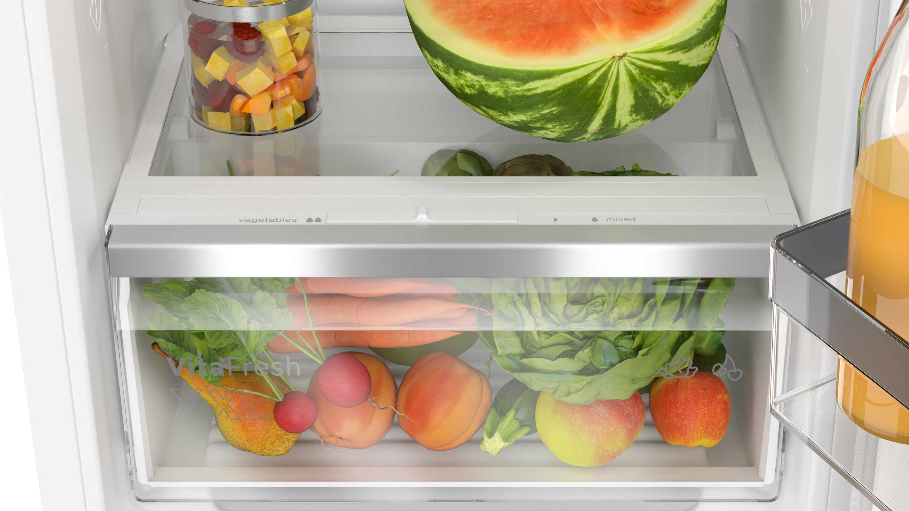 Eine Kühlschublade ist geöffnet, gefüllt mit Obst und Gemüse. Eine Wassermelone und ein Glas mit gemischten Früchten sind zu sehen.