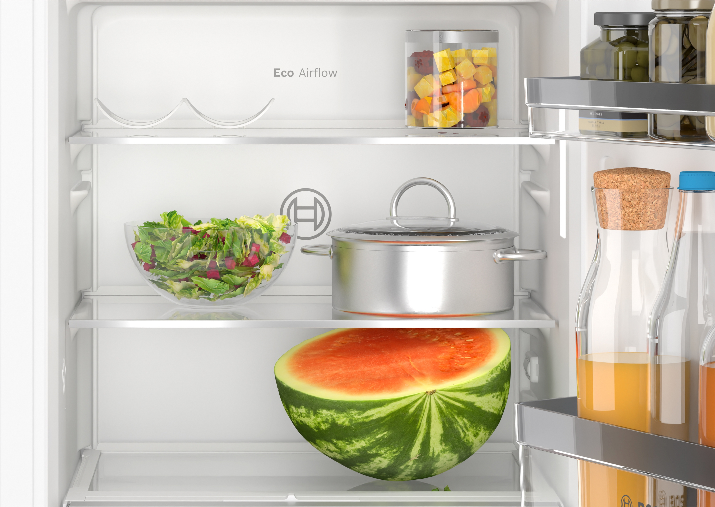 Kühlschrankinnenraum mit Lebensmitteln, darunter Salat, Wassermelone, Gläser und Flaschen. Das Label 'Eco Airflow' ist sichtbar.