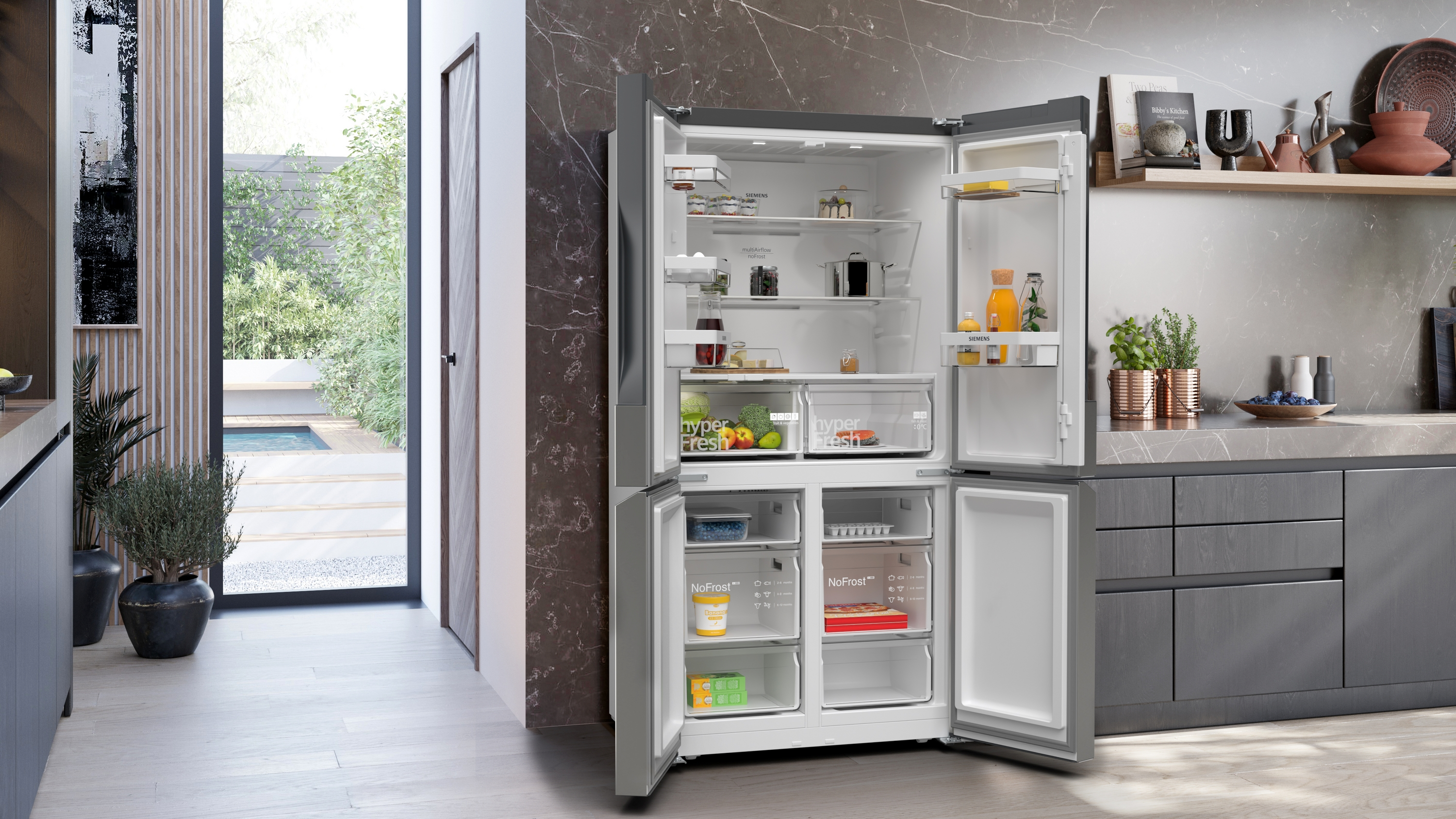 Offener Kühlschrank mit mehreren Fächern, Regalen, Schubladen und verschiedenen Lebensmitteln. Draußen ist ein Garten zu sehen.