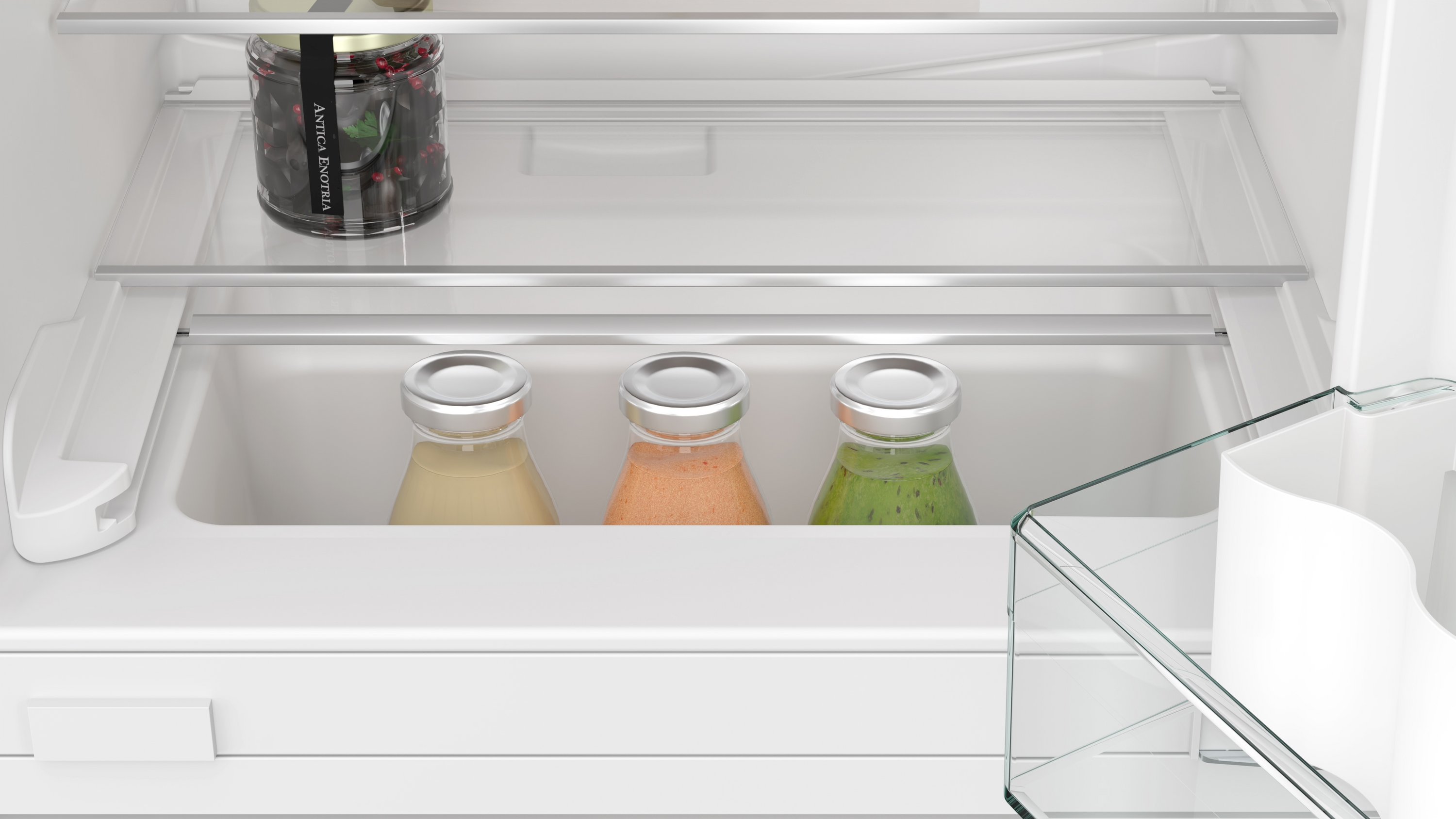In einem Kühlschrank: Gläser mit Saft und ein Glas Oliven. Weiße Regale und ein weißer Innenraum.