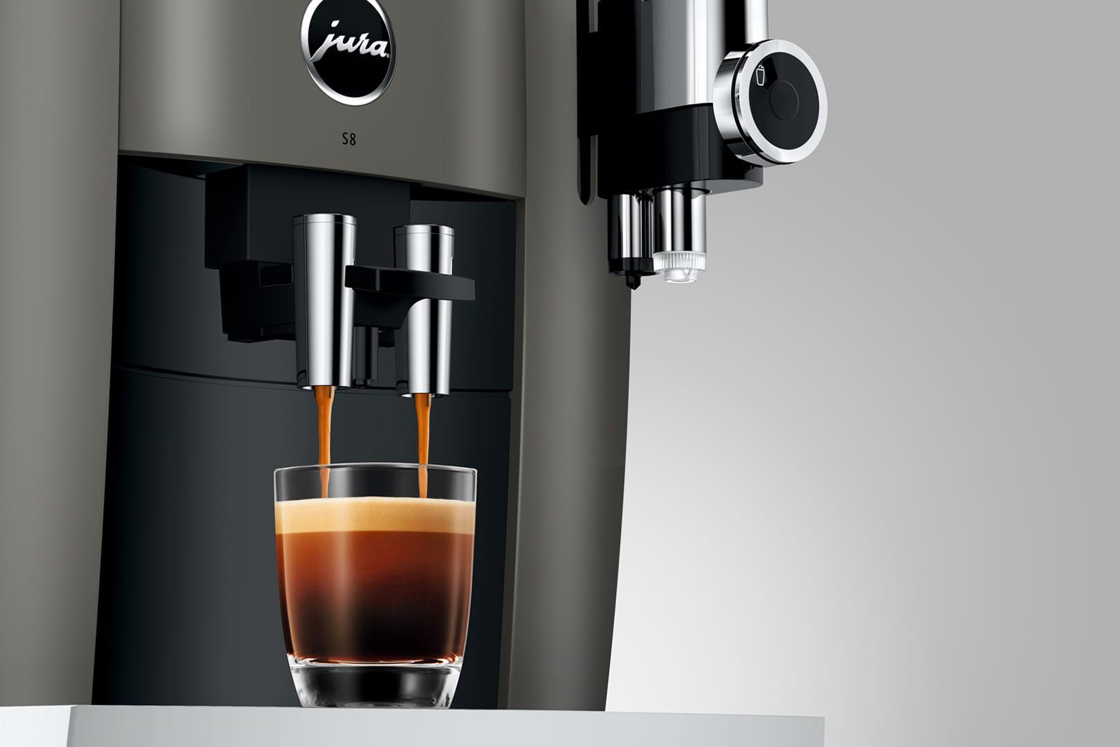 Kaffeemaschine, die Espresso in ein Glas ausgibt. Die Maschine ist grau mit schwarzem Bedienfeld.