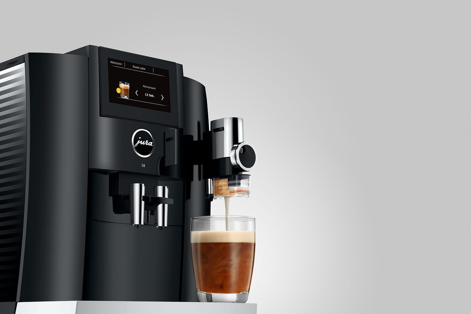 Eine schwarze Jura S8 Kaffeemaschine, die Kaffee in ein Glas ausgibt. Die Maschine hat einen Bildschirm.