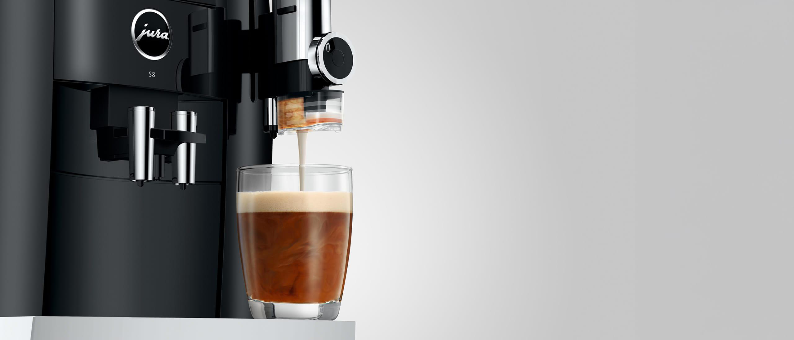 Schwarze Jura S8 Kaffeemaschine, die Kaffee in ein Glas ausgibt, auf weißer Oberfläche.