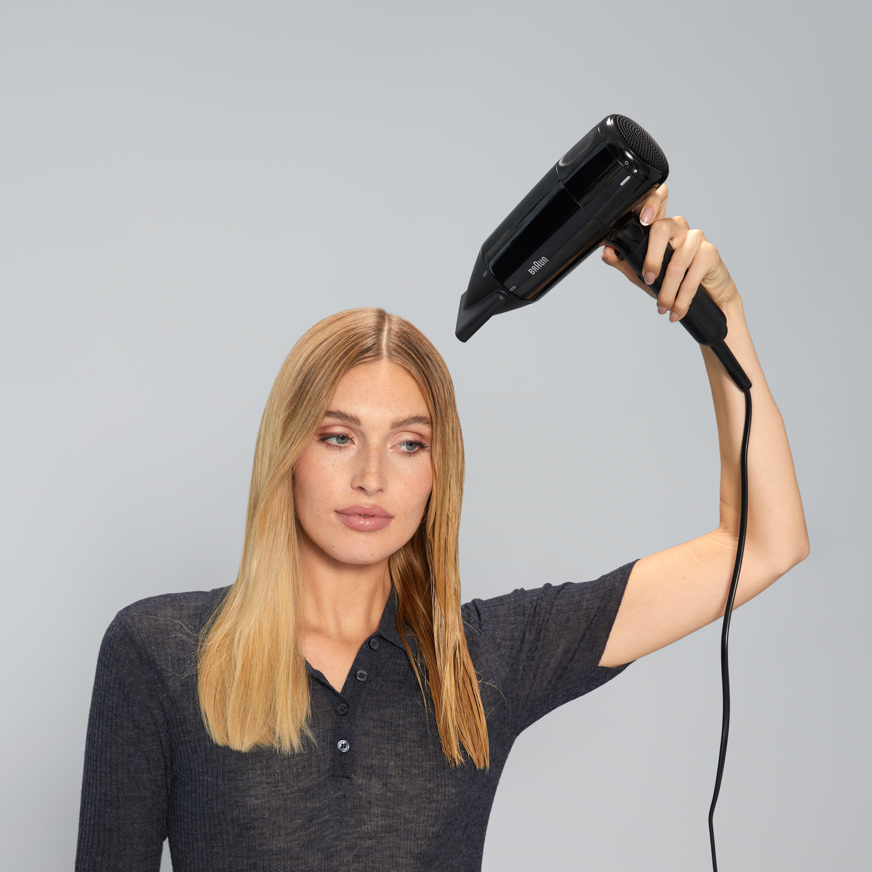 Frau benutzt einen schwarzen Haartrockner und hält ihn über ihr nasses Haar.