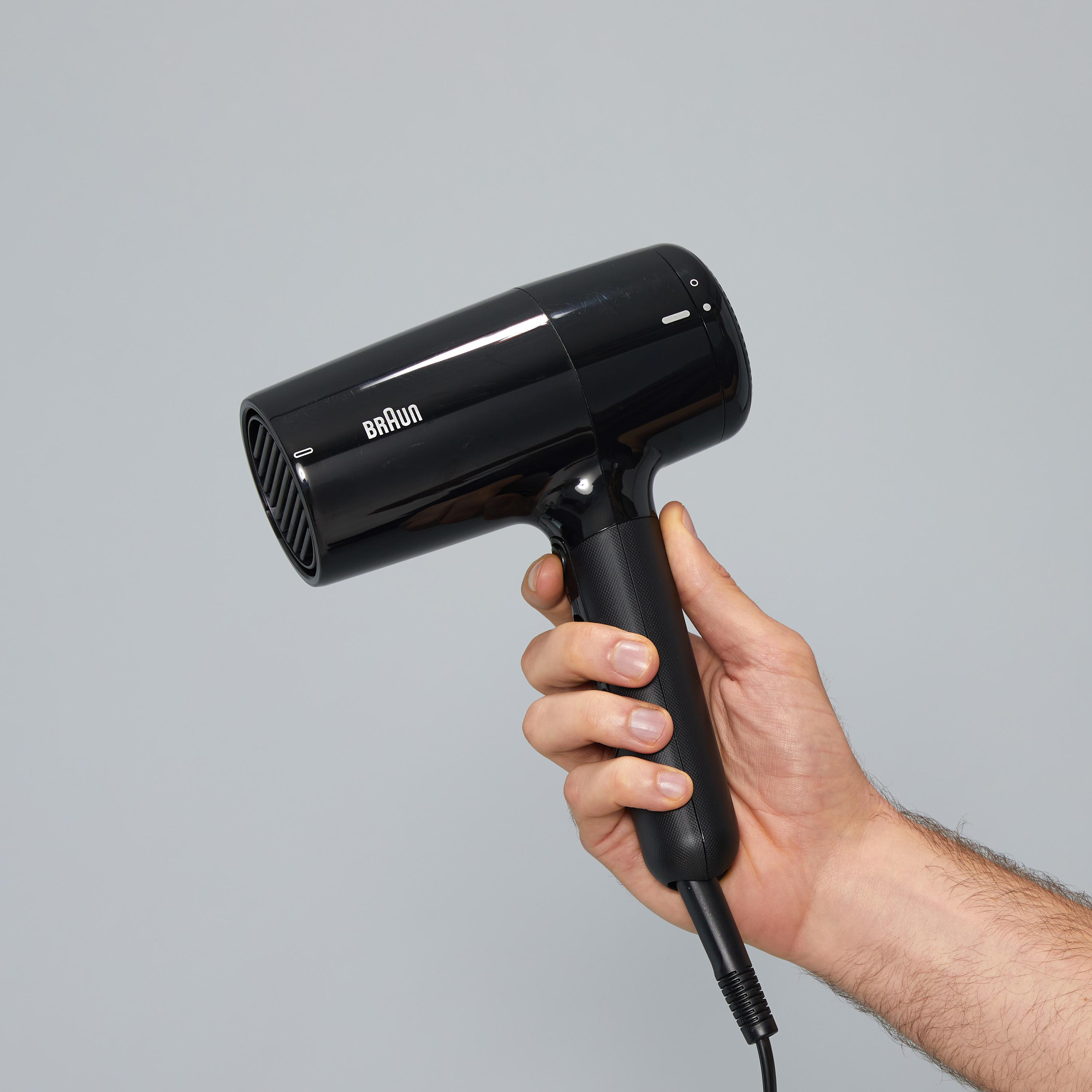 Schwarzer Braun-Haartrockner in einer Hand vor grauem Hintergrund. Das Produkt wird gezeigt.