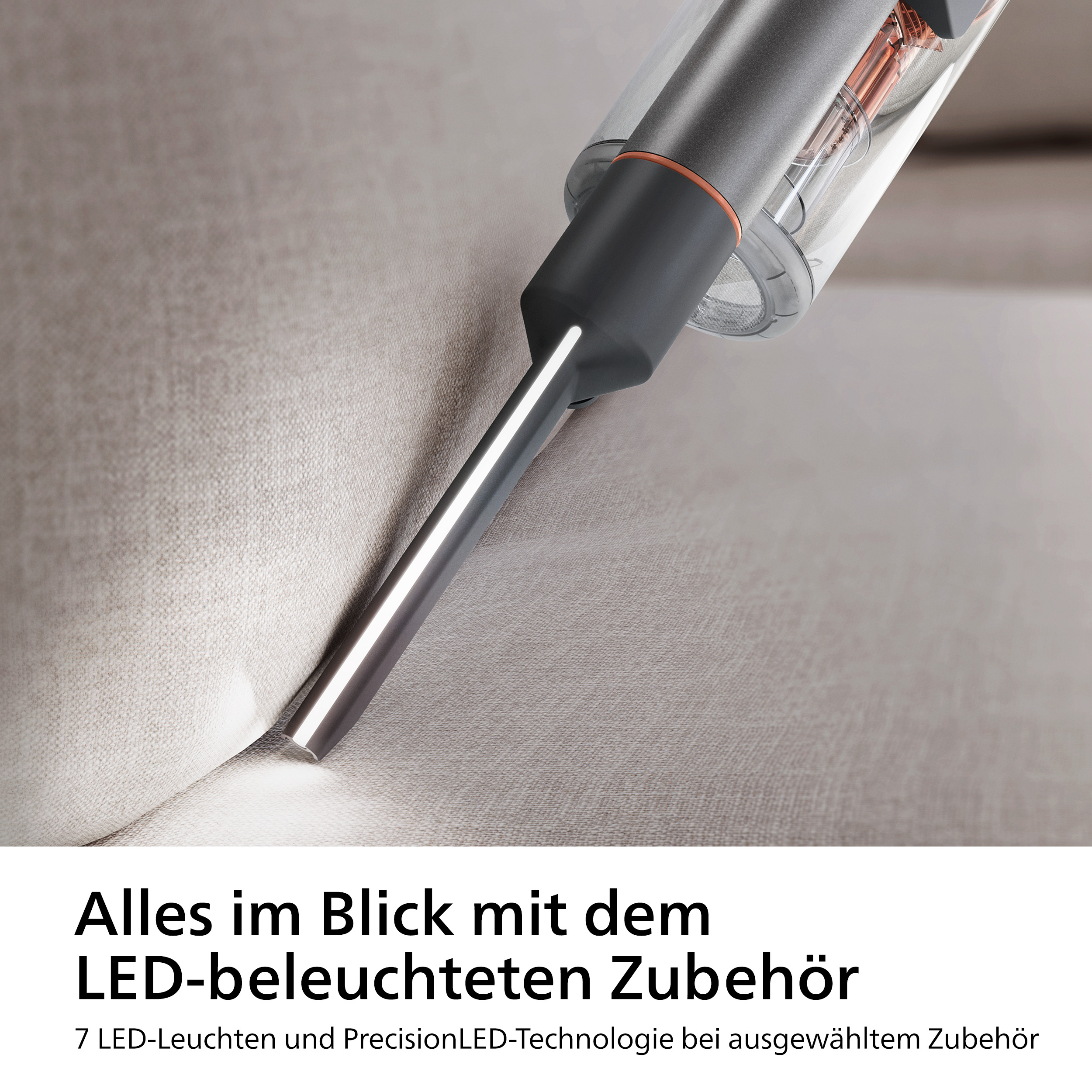 Staubsauger mit LED-beleuchteter Düse. Grau und orange. Nahaufnahme auf einem Sofa.