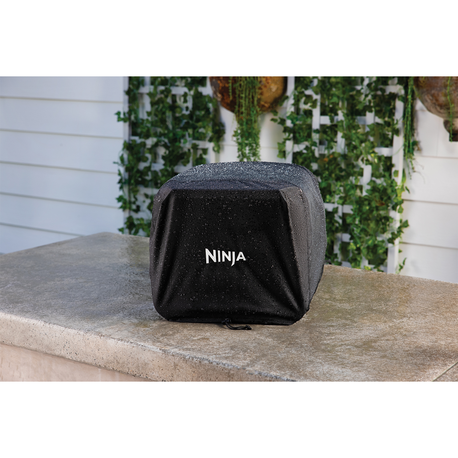 Copertura per grill Ninja nera su una superficie di pietra, con sfondo di vite verde.