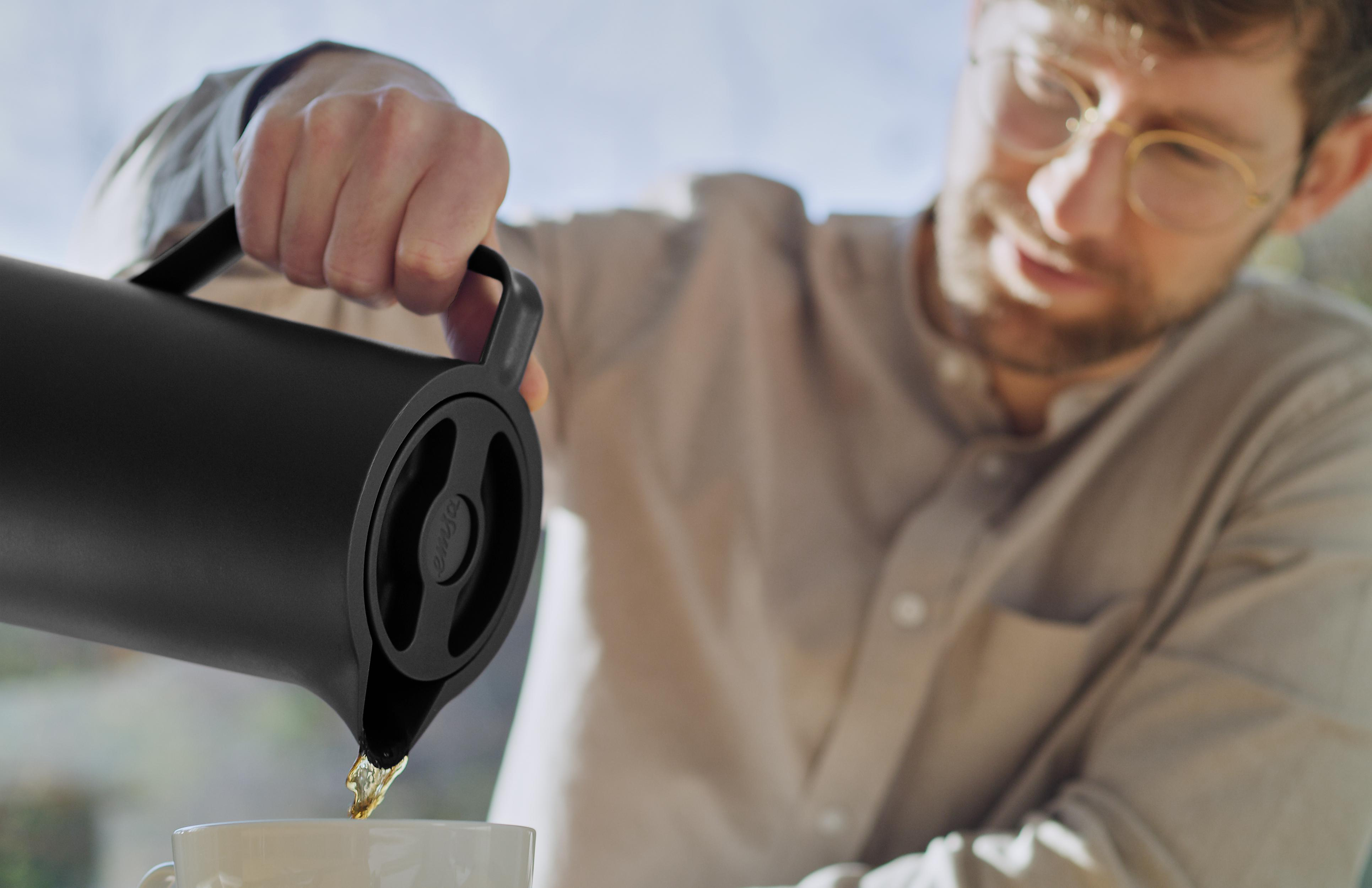 Person gießt Tee aus einer schwarzen Thermoskanne in einen weißen Becher.