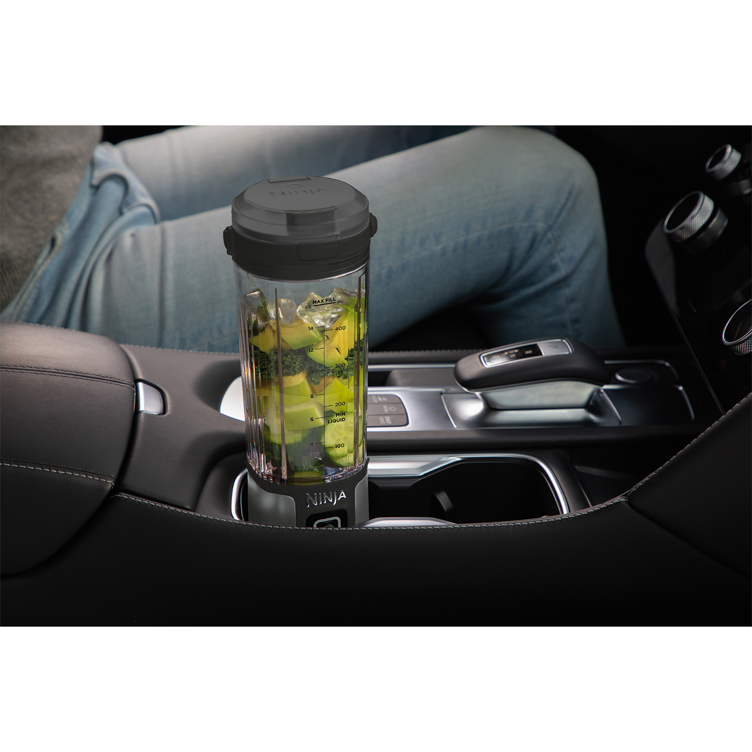 Frullatore Ninja in auto. Bicchiere del frullatore con contenuto verde e ghiaccio. Interno auto nero visibile.